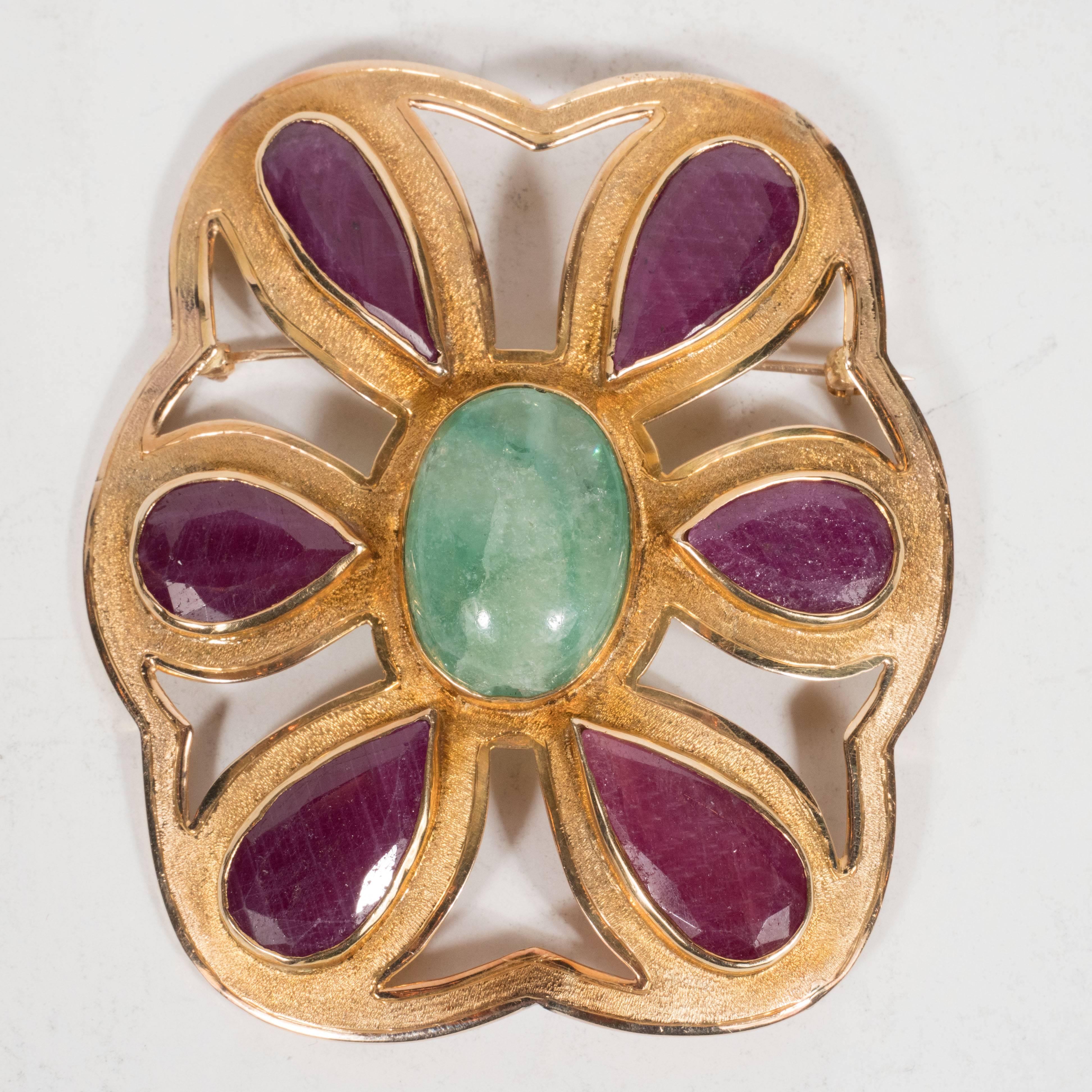 This superb Mid-Century Modernist brooch features six beveled pear cut rubies surrounding an ovoid cabochon emerald, set in brushed 14 karat yellow gold. The brooch includes scalloping along its sides and whale tale shaped cut-outs separating each