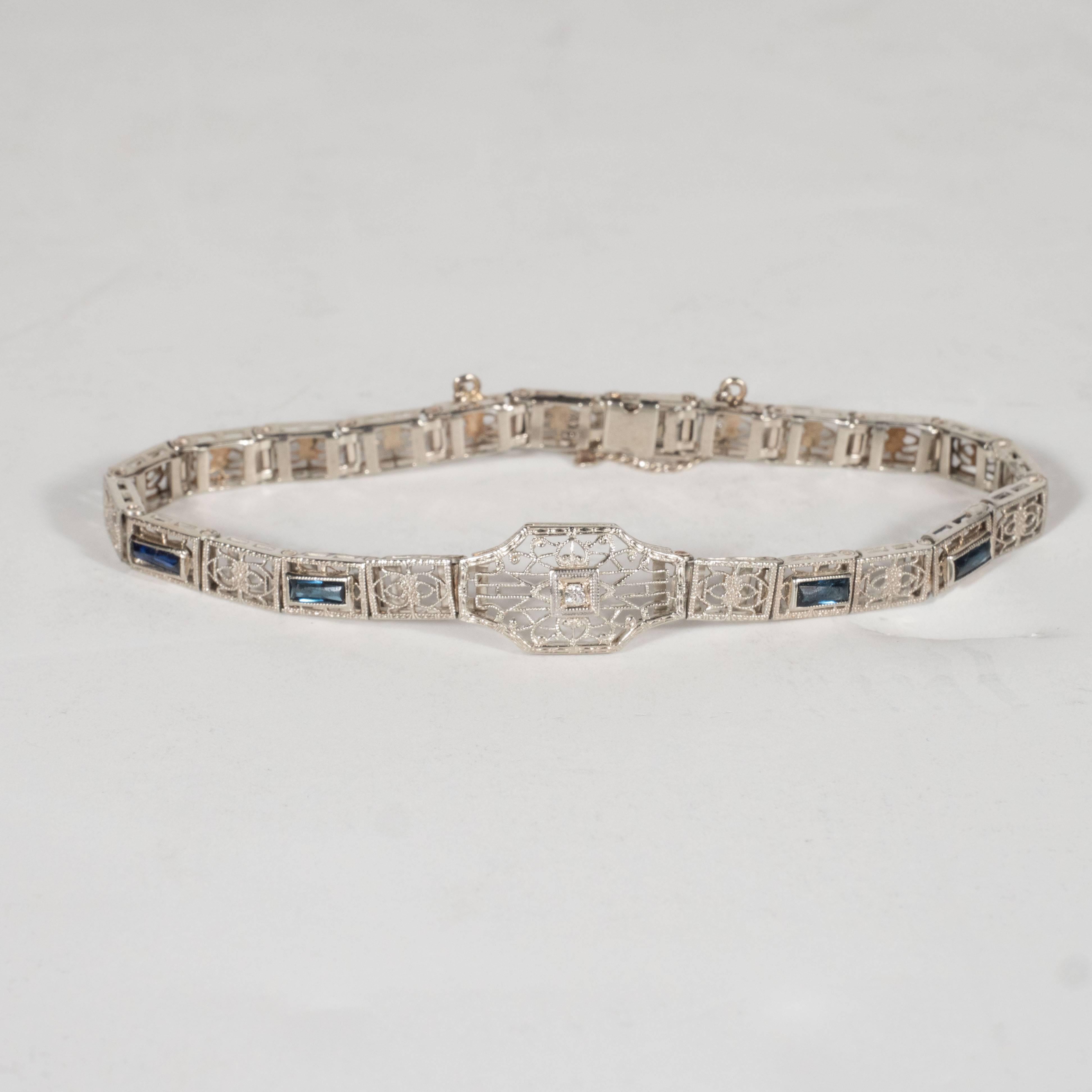 This sophisticated Art Deco tool & die bracelet is composed of 14k white gold stamped into perforated and intricately filigreed links. The central link features a brilliant cut diamond in a square setting surrounded by elaborate baroque designs.