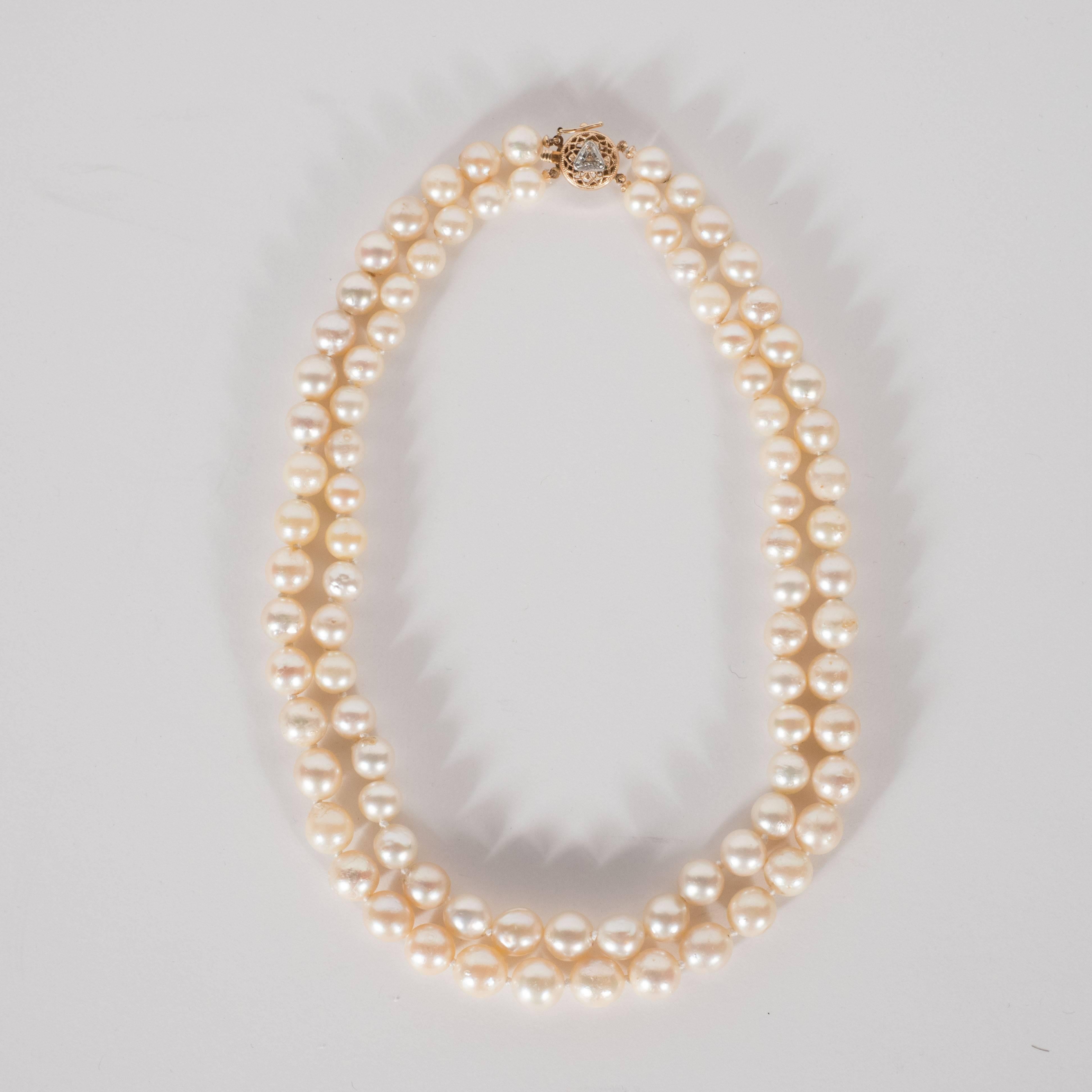 This elegant Baroque graduated double strand pearl choker necklace was realized in the United States, circa 1950. It features an exquisite circular gold filigree clasp with a trillion cut diamond in its center. With its classical and timeless form,