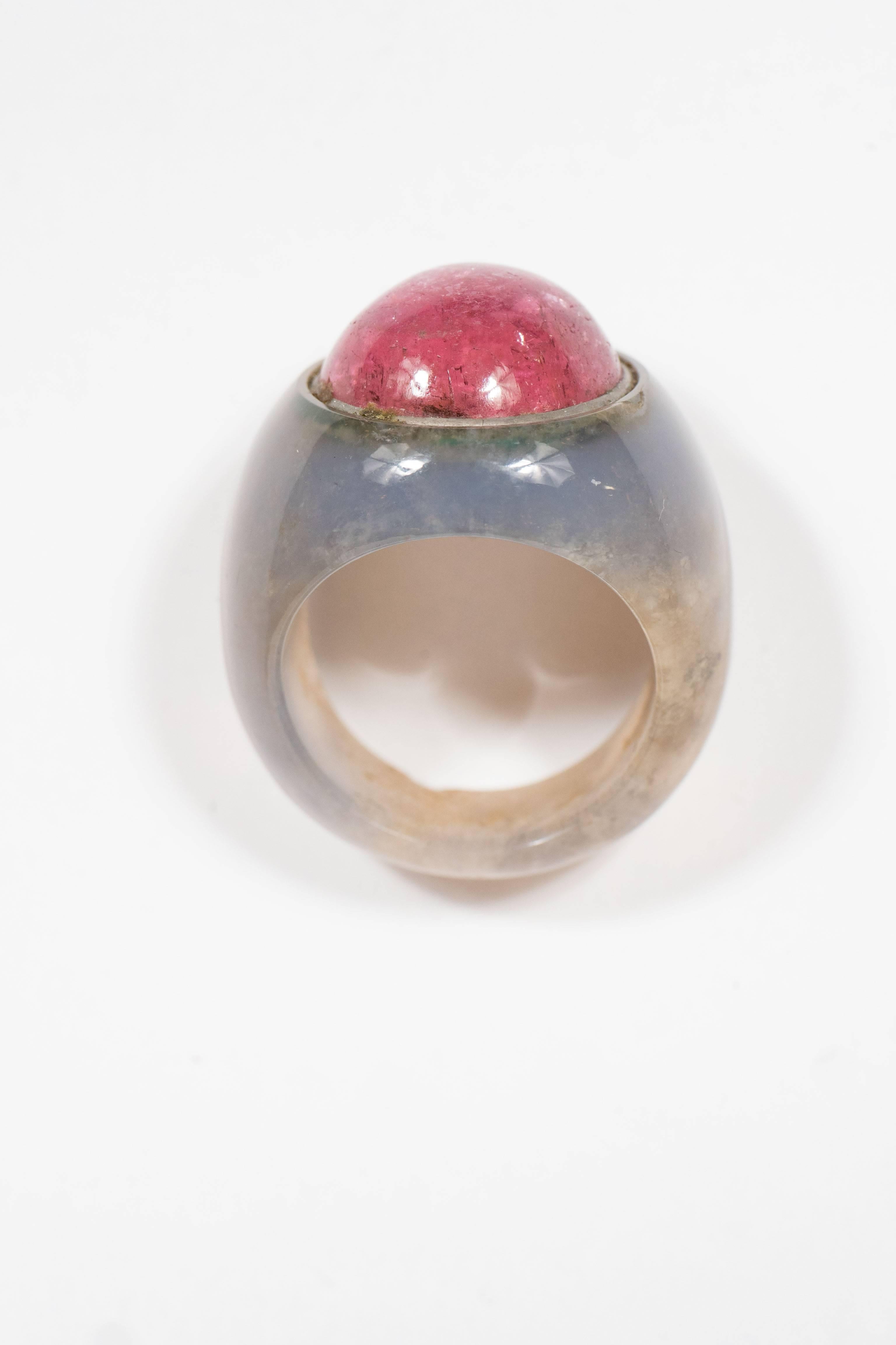 The mounting is composed of carved hard-stone, possibly a variety of chalcedony, centering one round cabochon pink tourmaline measuring approximately 14.8 mm. Ring is a size approximately 7. It is in excellent condition.
From the estate of Maxine