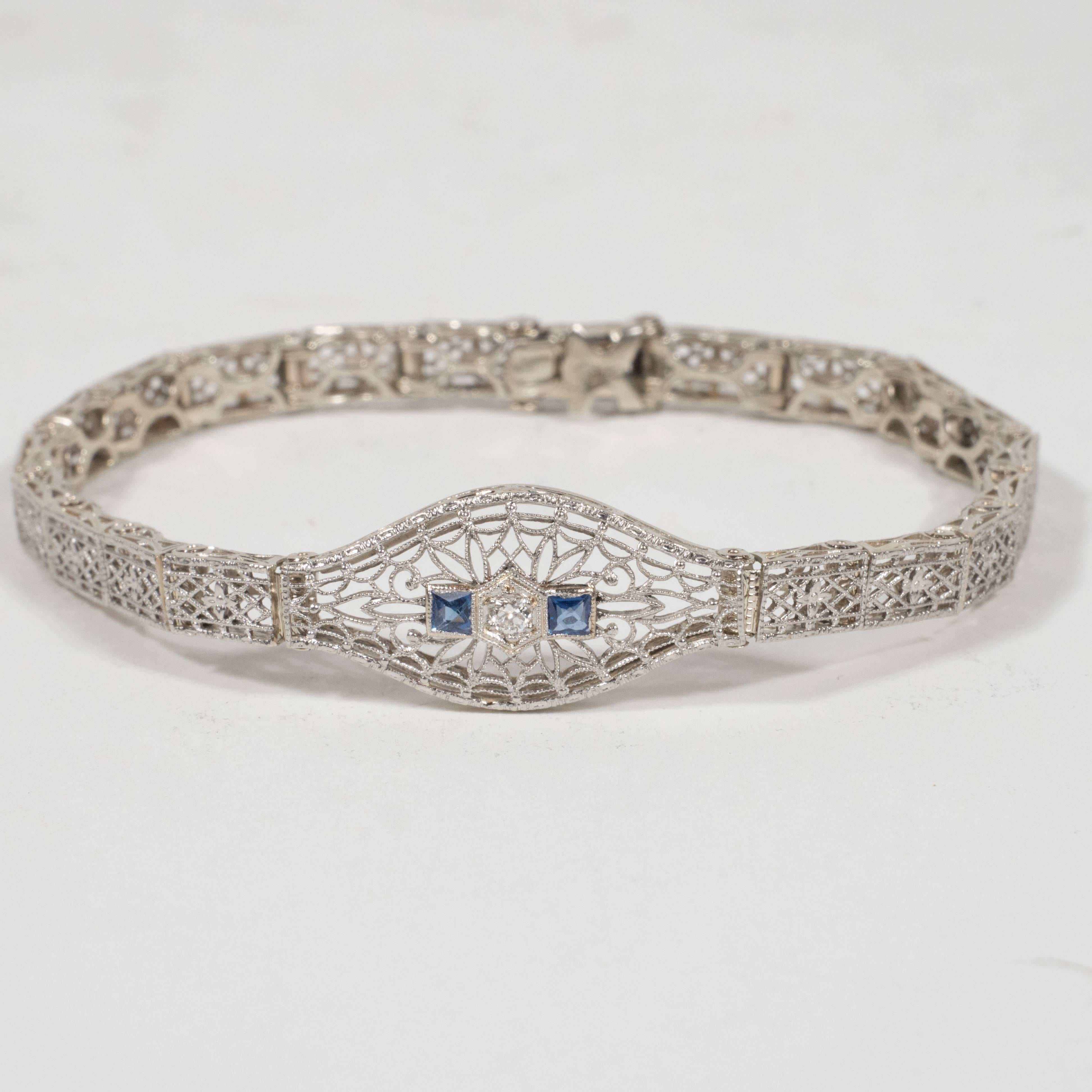This gorgeous Art Deco bracelet features a central three point old mine cut diamond placed in a hexagonal shaped setting which is flanked by two square cut synthetic sapphires on either side. The central link offers a wealth of baroque patterns,