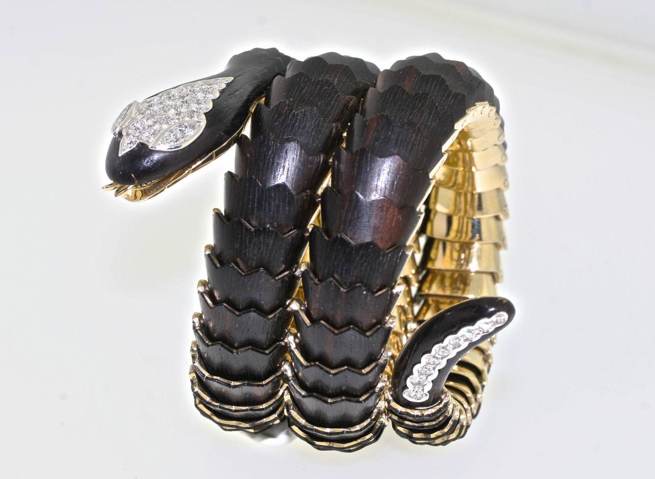 Illario bracelet designed as a series of articulated ebony wood and gold sections riveted together at each joint create a seamless flow of silky scales which coil around the wrist to form a sinuous serpent. The diamond-set head and tail add