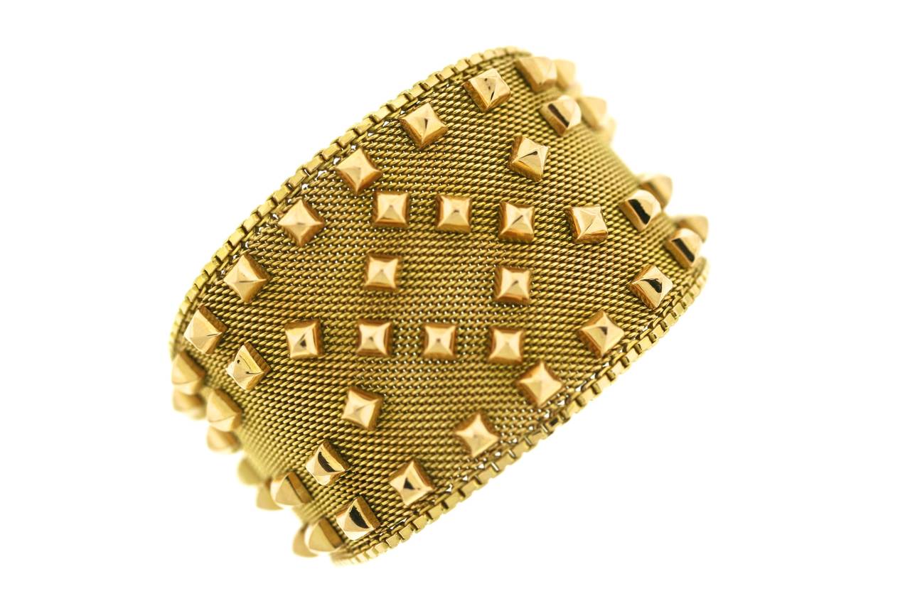 18k gold cuff bracelet designed as a flexible mesh weave with a double functional buckle closure. Studded with golden pyramids this piece is a sophisticated statement of style with both fashion forward appeal as well as a bit of punk throwback mixed