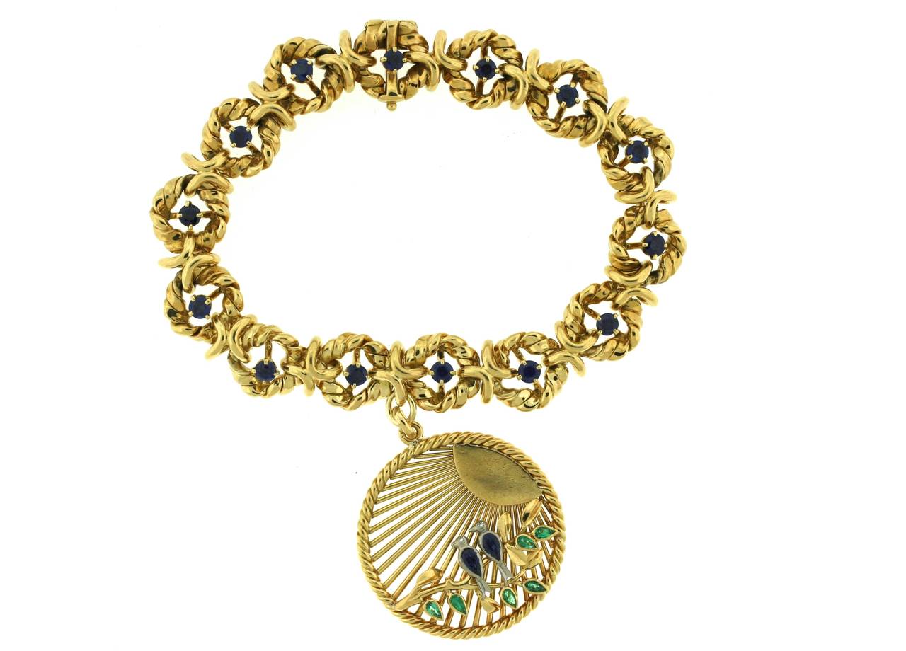 Van Cleef & Arpels Paris 18k gold bracelet designed as circular links of twisted gold each centering a sapphire suspending a charm depicting two sapphire and diamond lovebirds on a branch of emeralds. Bracelet is 7.5