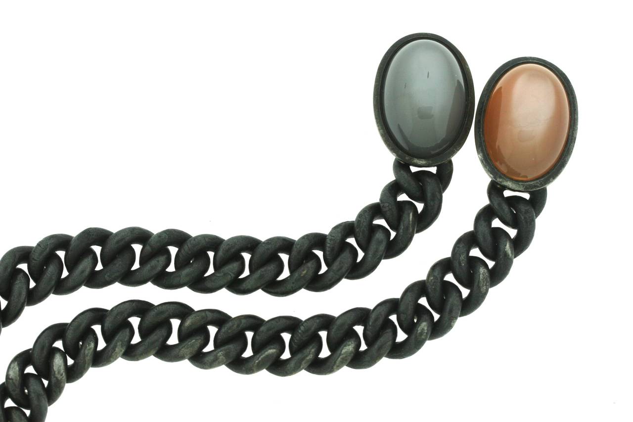 A pair of blackened steel bracelets capped with two large, grey and orange moonstones. While the orange moonstone is backed with 18k rose gold, the grey moonstone is backed with 18k white gold. The bracelets link seamlessly together into a choker;