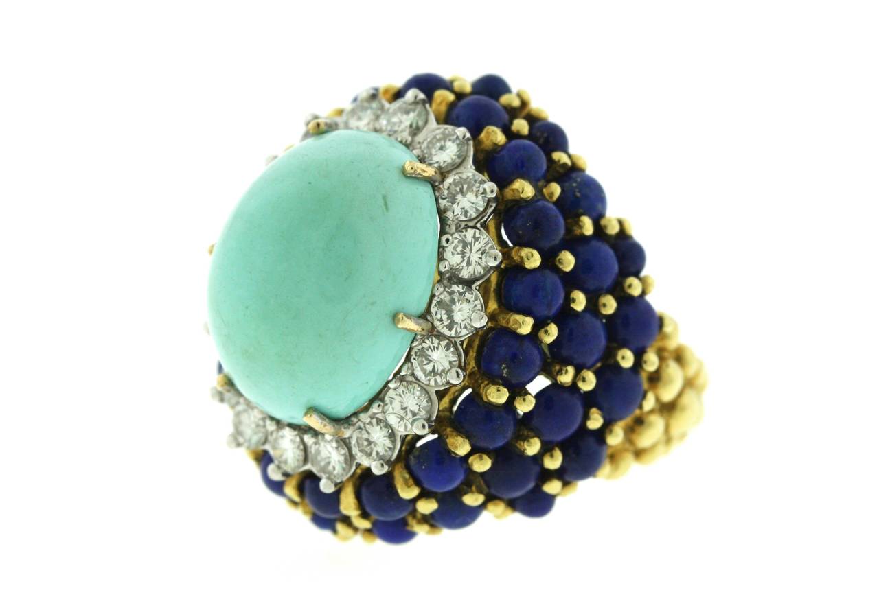 La Triomphe 18k gold bombe cocktail ring centering an oval turquoise stone of Persian origin surrounded by eighteen round brilliant cut diamonds totaling approximately one carat. Balls of denim blue lapis and gold surround the diamonds and continue