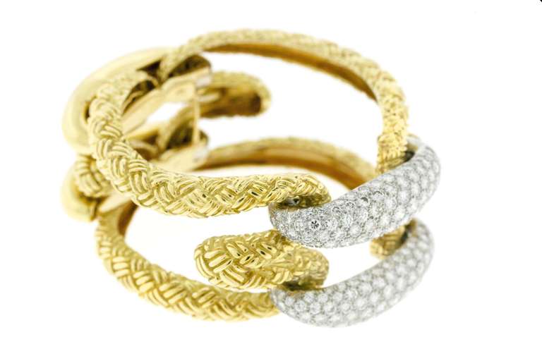 Comprised of two rope-like plaques in a textured woven gold pattern; held together by a pair of rounded diamond set links in the front and rounded gold links that conceal the clasp. This is an example of 1970's design in which the negative space is