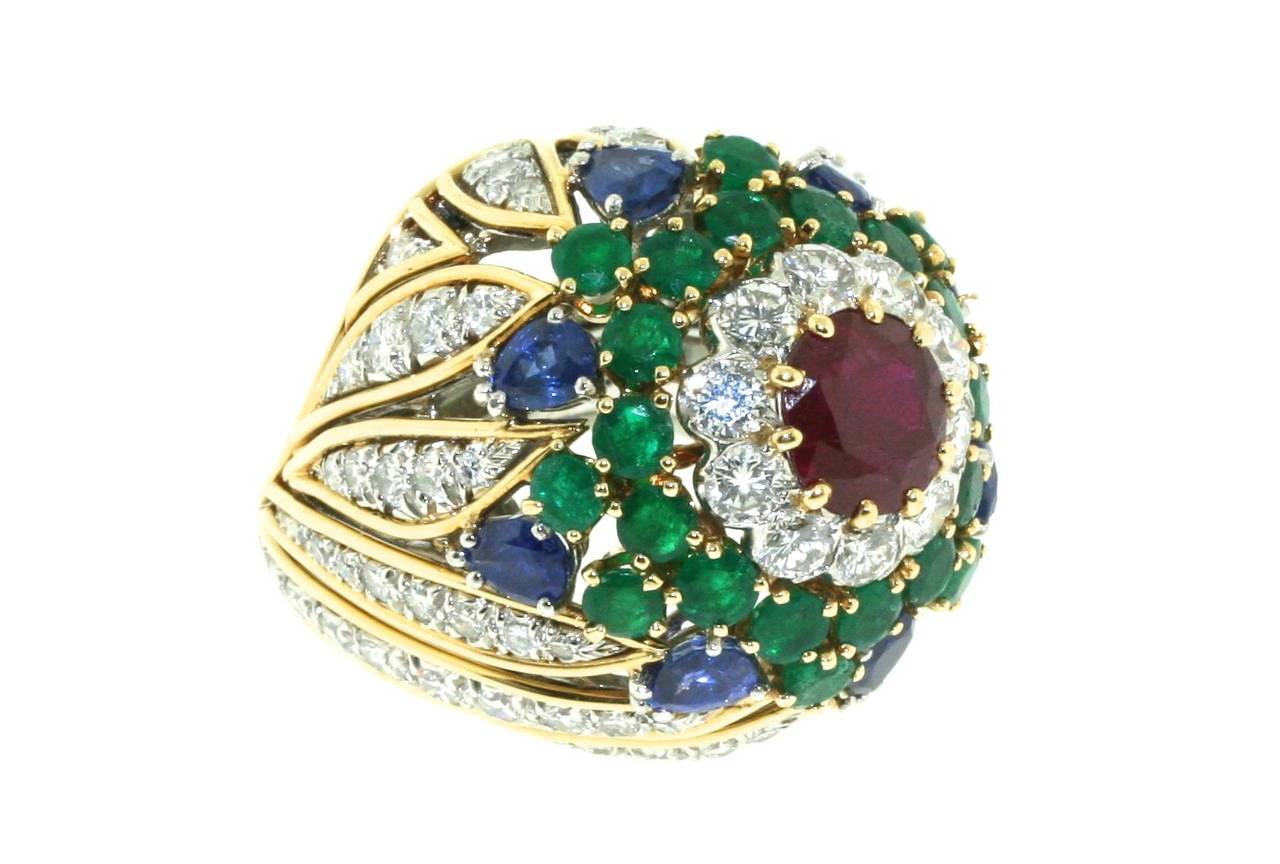 David Webb 18k gold and platinum bombe-shaped cocktail ring centering a 1.5 carat faceted round Burma ruby surrounded by 10 round brilliant diamonds, 22 emeralds, 8 pear shaped sapphires, and a 72 additional diamonds in a swirled patter around the
