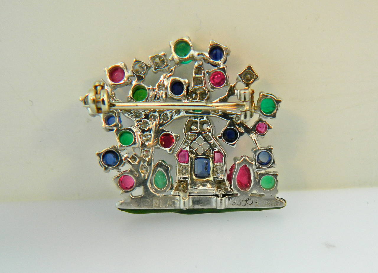 A Platinum, Diamond, Enamel and Multi Gem Brooch by Raymond Yard, 
depicting a church and overarching tree.  Set with diamonds, round mixed cut, round cabochon cut and carved rubies, sapphires, emeralds and garnets, the base in opaque green enamel.