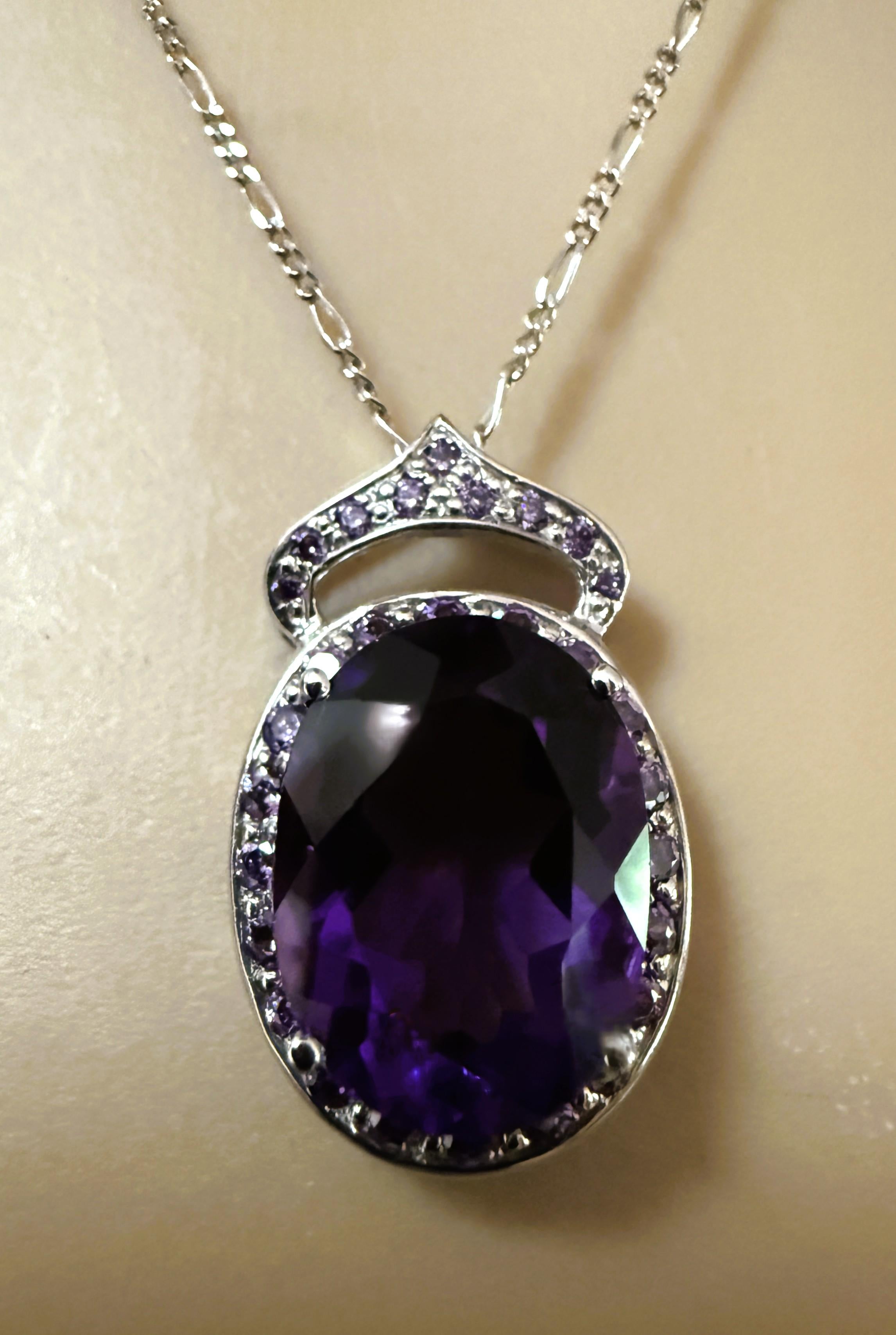 Der Stein stammt aus Brasilien und ist einfach exquisit. Der Stein ist ein Amethyst mit ovalem Schliff und hat 8,0 Karat. Er misst 16 x 12 mm und ist von lila Saphiren im Diamantschliff umgeben.  Es hat auch einen Heiligenschein, der mit