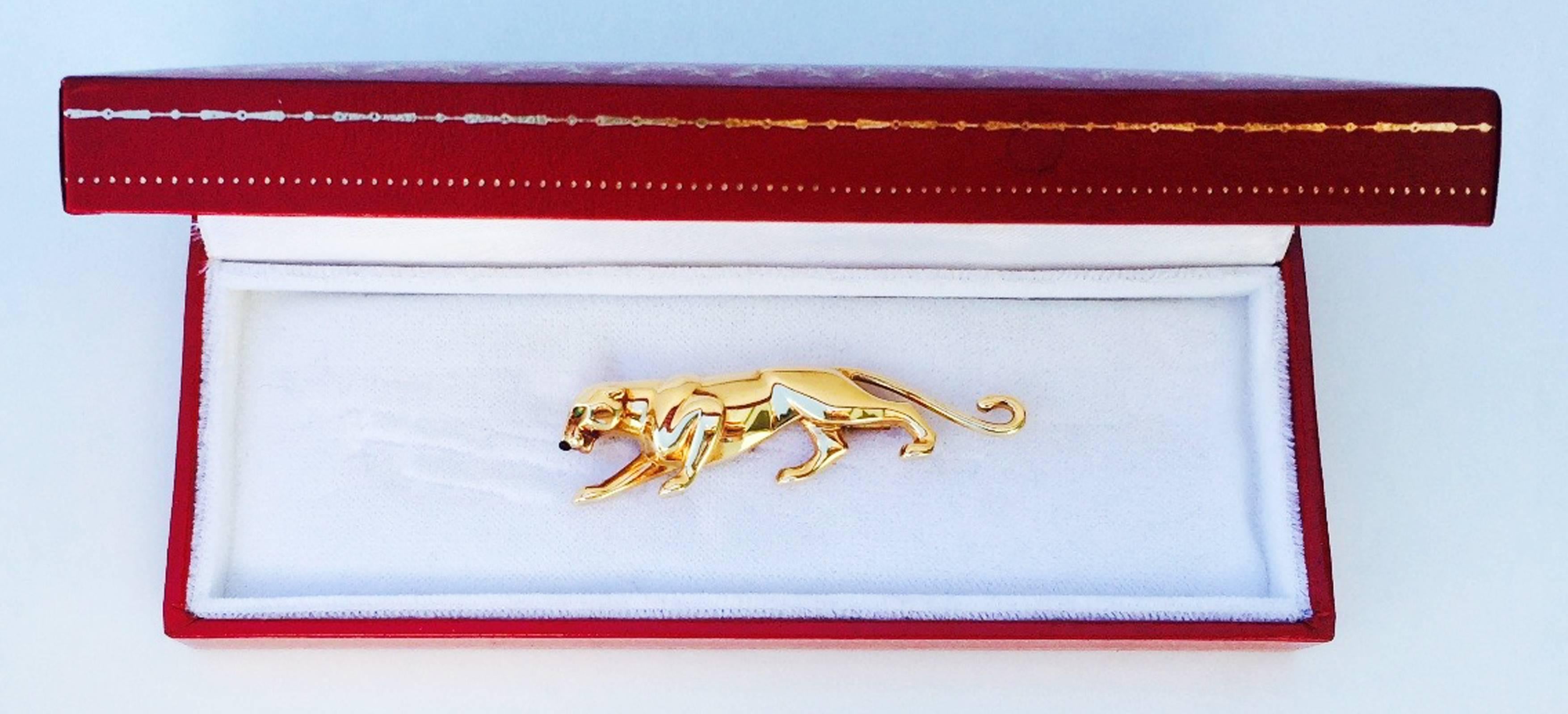 A fine Cartier Paris panther brooch. Signed and hallmarked yellow gold item features emerald eyes and black onyx nose. Original locking clip pin back and signature box included. Pristine.