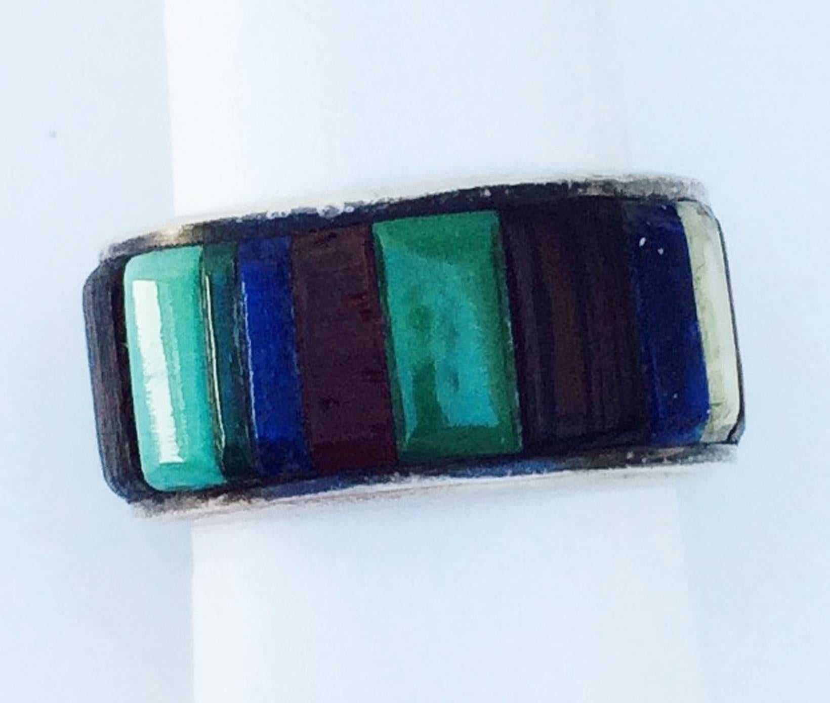 A fine and rare Charles Loloma inlaid band ring. Impressive signed sterling silver item with 14k yellow gold, turquoise, Lapis, coral, wood etc. circling the entire ring. Ring size 8.5.