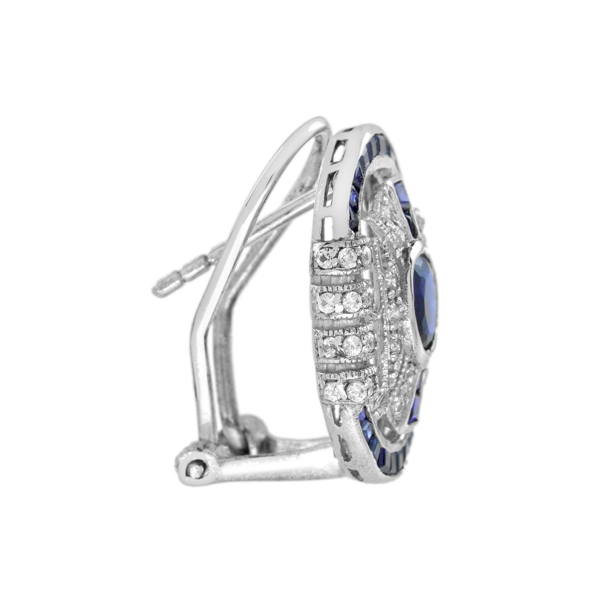 Une paire de boucles d'oreilles d'inspiration Art déco qui attire toute l'attention sur les saphirs bleus de forme ovale placés au centre. Ornées d'environ 0,41 carats de diamants (au total) et de saphirs bleus de taille française, ces magnifiques
