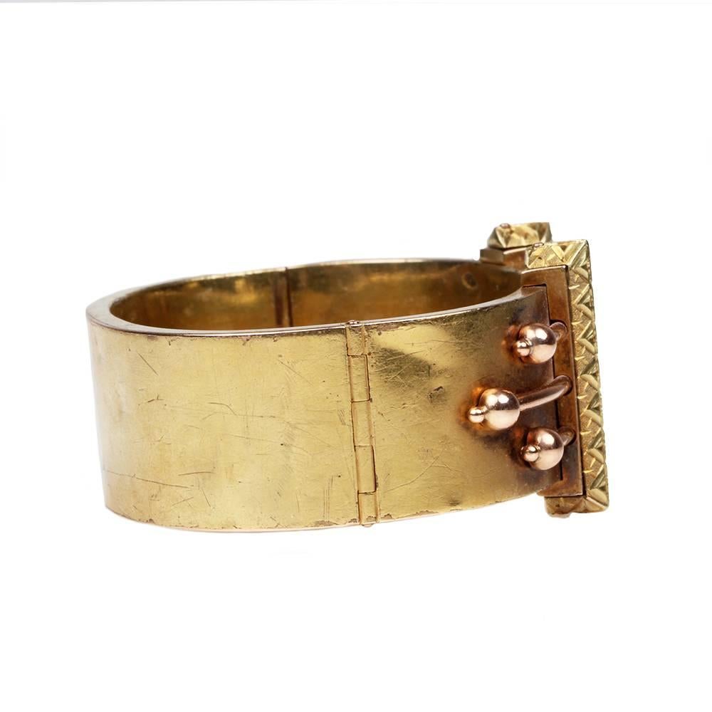 Victorian era bangle bracelet. Crafted in the Etruscan Revival design motif.  In 14k rose and yellow gold. English in Origin. Circa 1860. 

Hinged at side with push button closure, with safety chain attached. Inner circumference measures