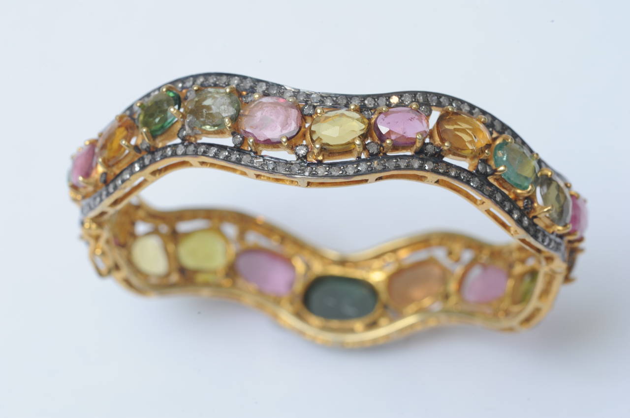 Oval shaped hinged bracelet with push clasp and figure-8 safeties.  One side features large faceted oval tourmalines in pink, yellow and green, and the reverse with smaller sized tourmalines bordered with pave' set diamonds in oxidized sterling,