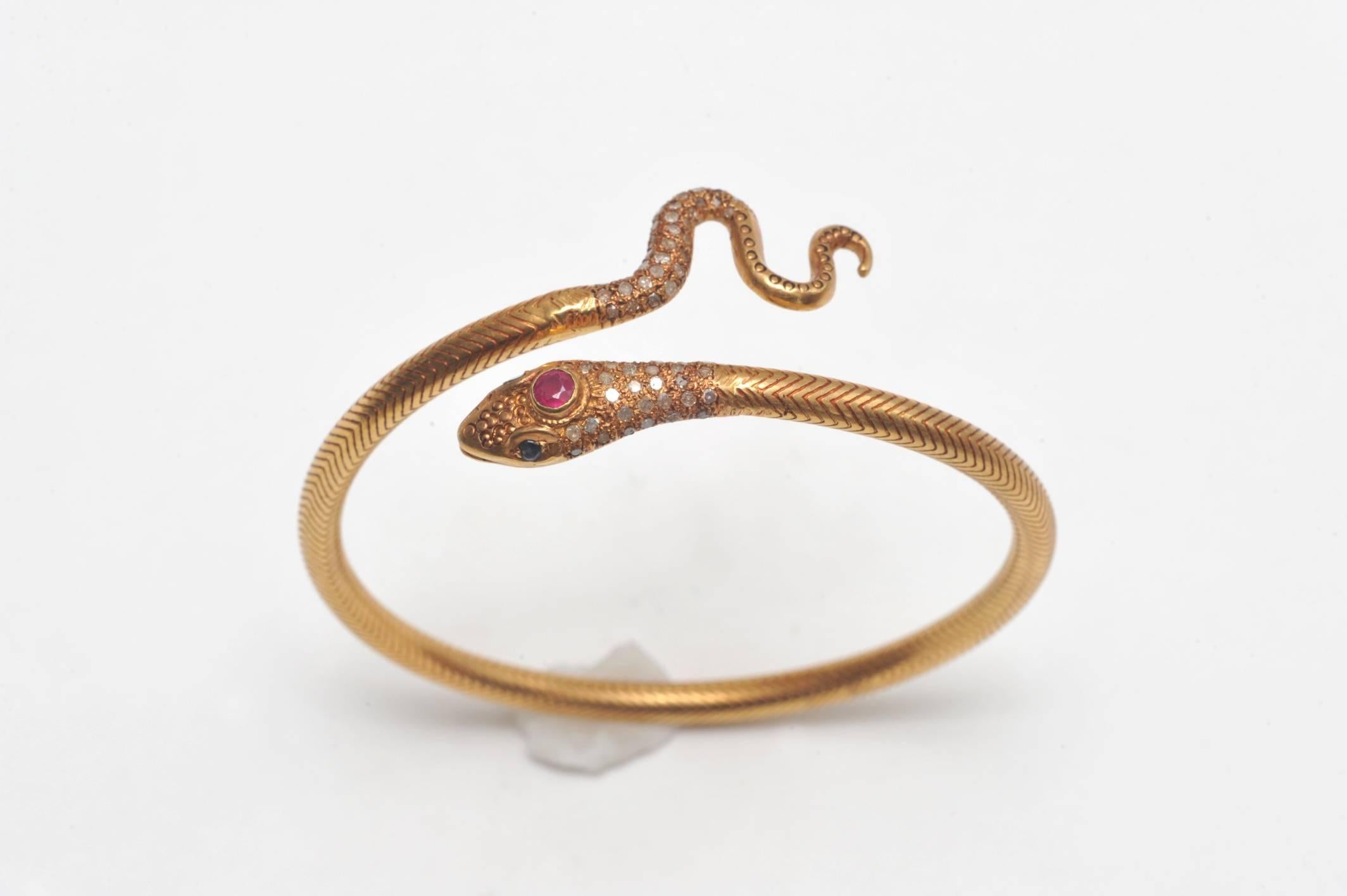 An exquisite snake bracelet of densely woven 18K gold in a herringbone pattern with pave`-set diamonds at the top of the head and the tail.  Has a faceted ruby third eye and faceted blue sapphire eyes.  Easy to get on as it has a bit of flex for a