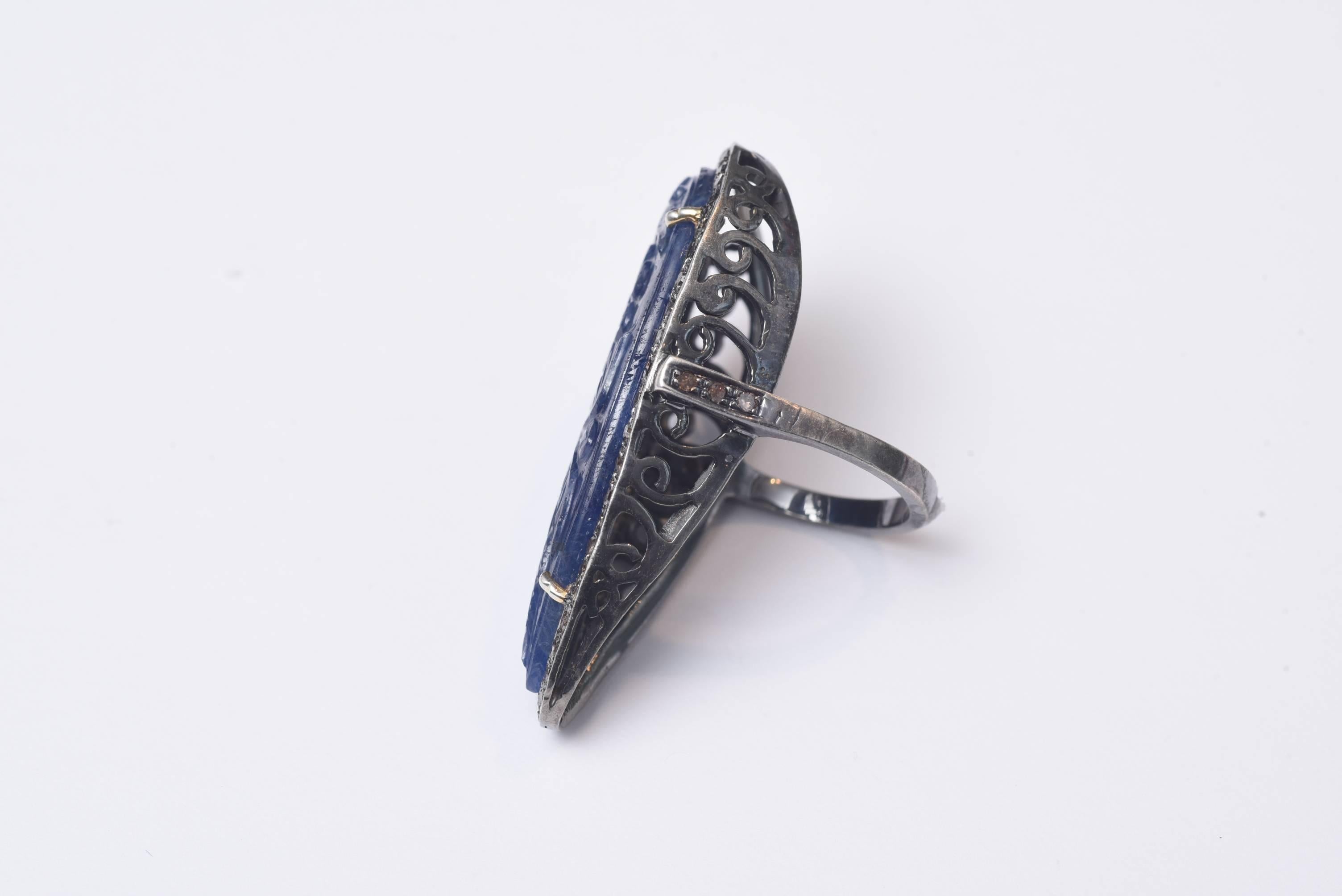 A lovely blue sapphire as it's found in its natural state and then hand carved with a floral design and even a much subtler carving on the inside.  Bordered in diamonds set in oxidized sterling.  Ring size is 8-8.25.  Carat weight of sapphire is