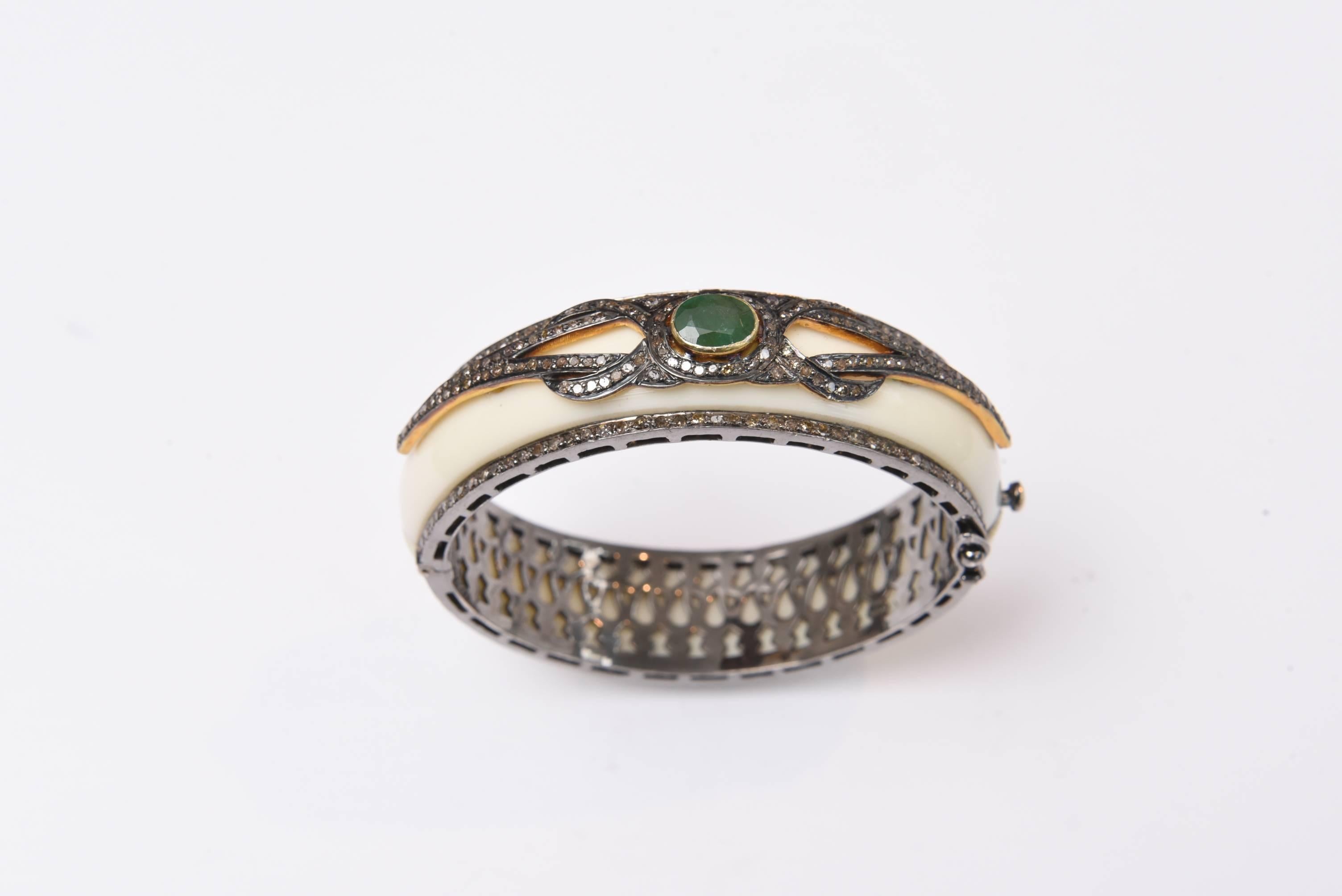 Diamonds and a faceted emerald adorn the top of this white bakelite cuff bracelet.  The pattern is in a stylized square knot.  Set in oxidized sterling silver.  The oval shape keeps the workmanship on the top of the wrist.  Carat weight of diamonds