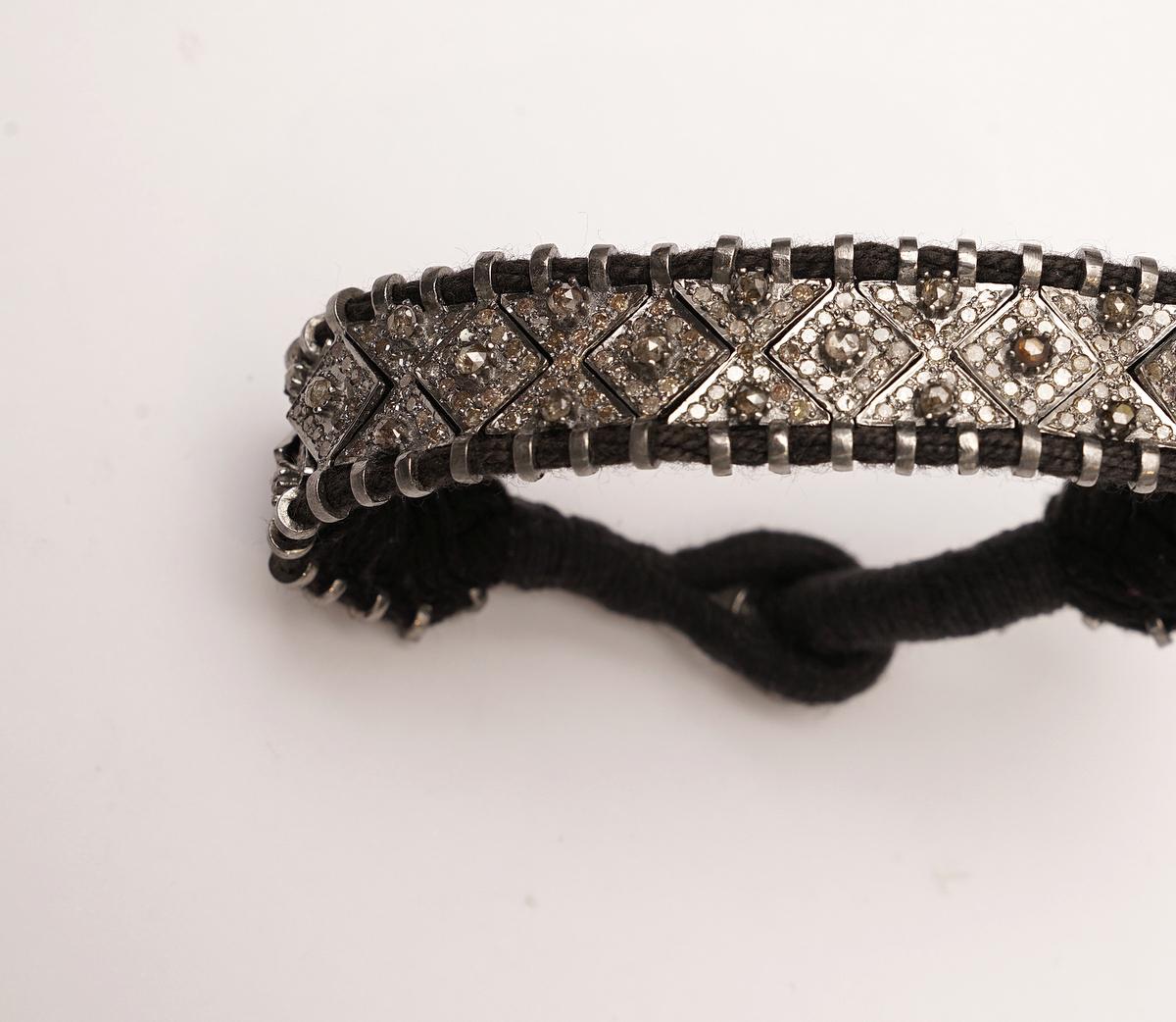 Articulated segments of pave`-set diamonds with bezel set champagne diamonds, all mounted in oxidized sterling silver links and threaded onto a woven black cotton cuff.  Button and loop closure also with pave`set diamonds.  Carat weight of diamonds