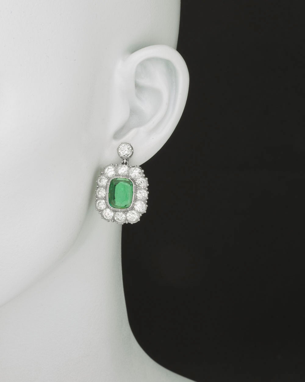 Emerald and diamond drop earrings, showcasing two cushion-shaped emeralds weighing approximately 3.42 total carats, surrounded by circular-cut diamonds weighing approximately 10.62 total carats, mounted in platinum, with posts. 1.25