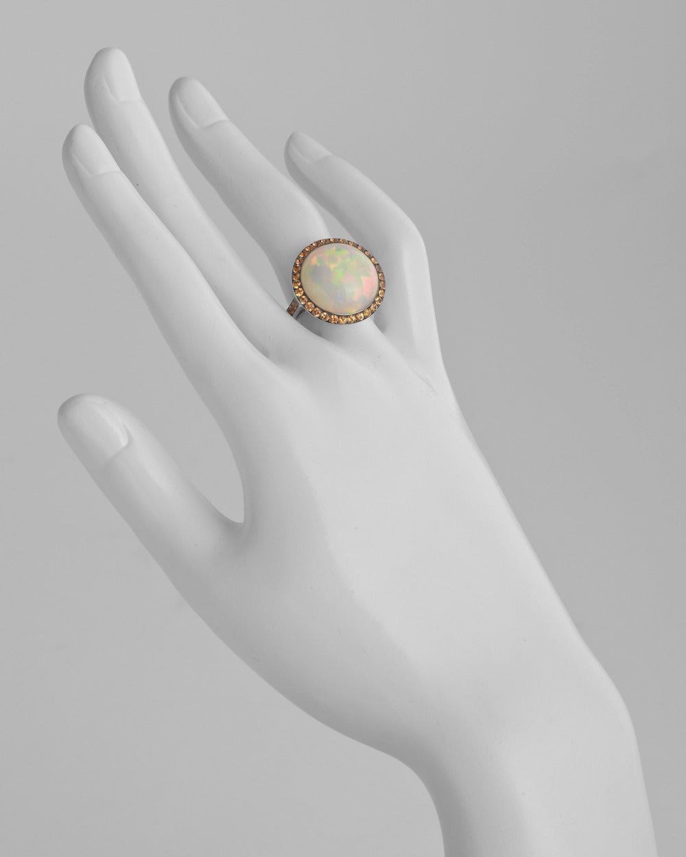 Round cabochon-cut opal cocktail ring, with a pavé orange sapphire surround and partway pavé orange sapphire band, the opal weighing 13.90 carats (18mm diameter) and 42 sapphires weighing 1.17 total carats, mounted in 18k white gold. Designed by