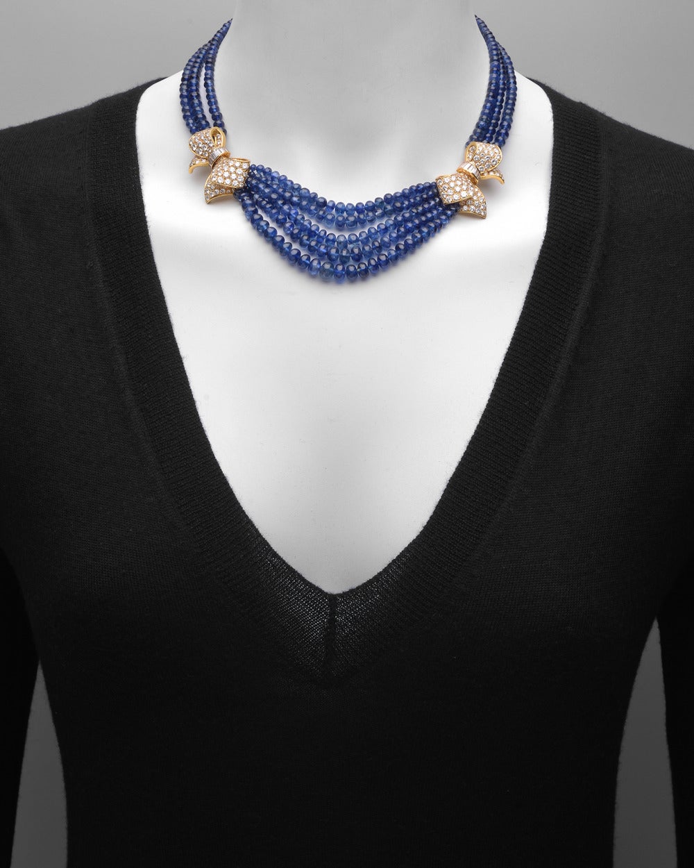 Multi-strand sapphire bead necklace, designed with a central section of five sapphire bead strands to two diamond-set bows in 18k yellow gold, the back with two sections of three sapphire bead strands secured by a pave-diamond set clasp in 18k