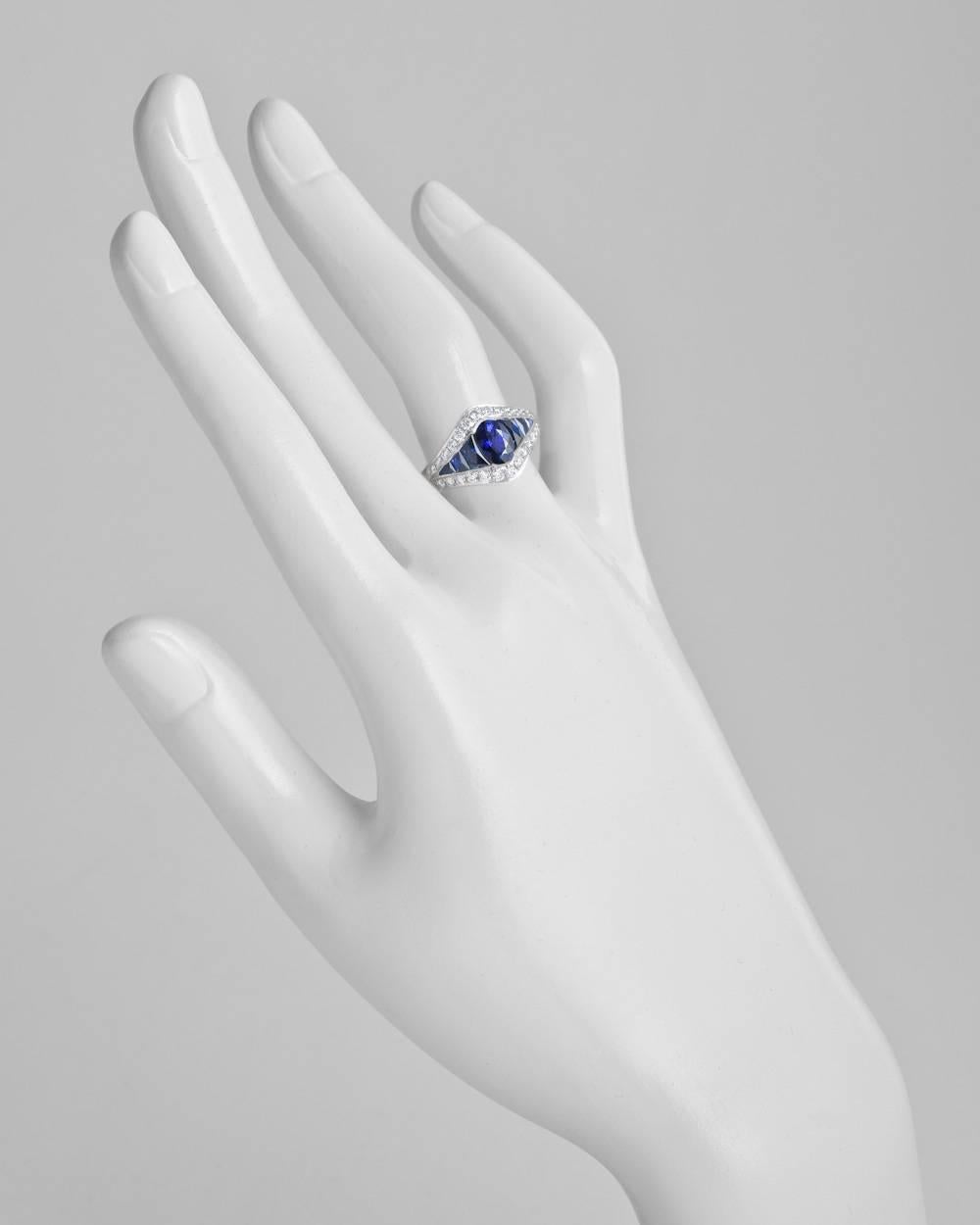Sapphire and diamond three-row dress ring, showcasing a larger oval-shaped sapphire at center flanked by smaller calibre-cut sapphires, within a near-colorless round brilliant-cut diamond surround, mounted in platinum. Oval-shaped sapphire weighing