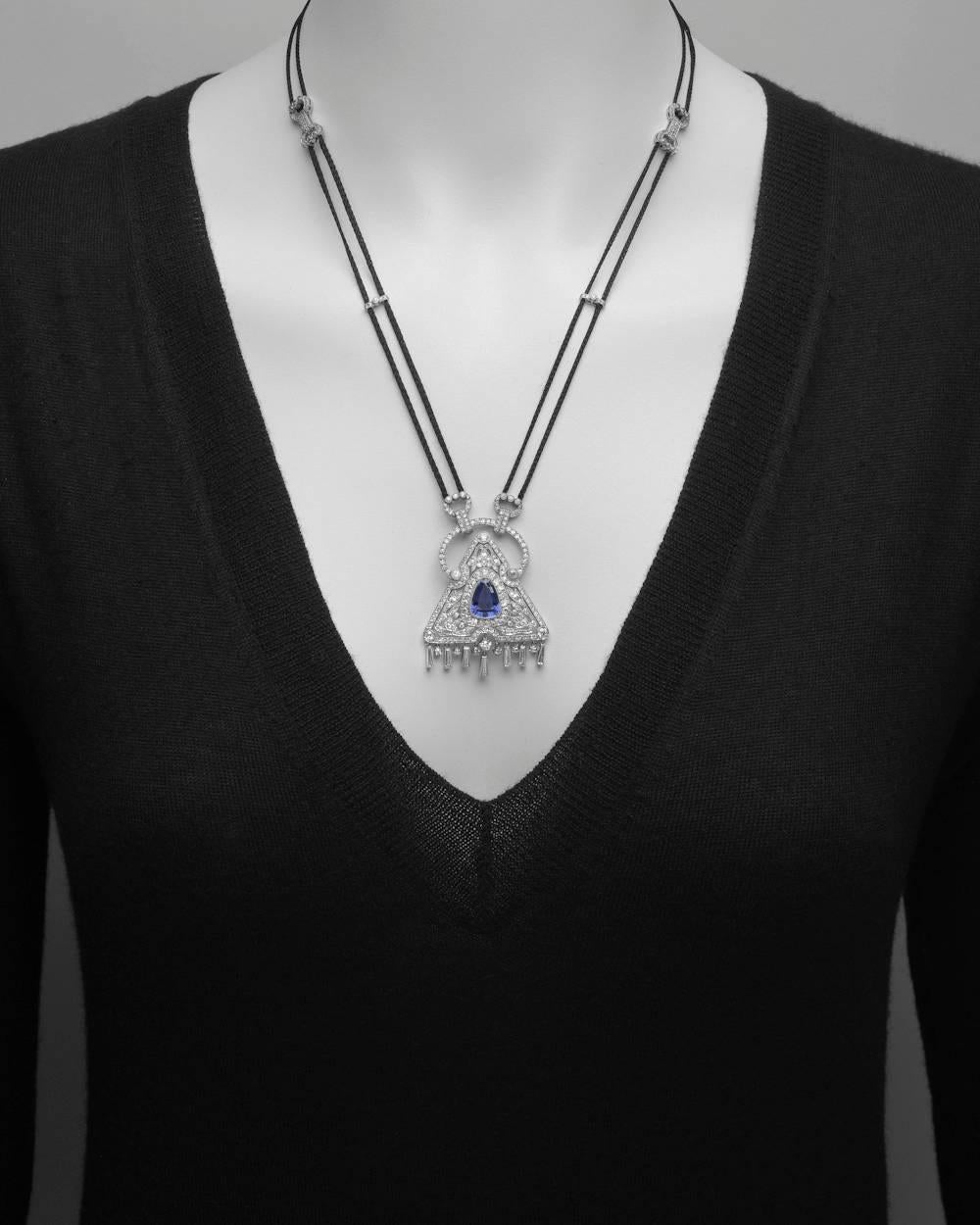 Sapphire and diamond pendant necklace, centering a triangular-shaped step-cut natural sapphire weighing 5.53 carats, surrounded by circular-cut diamonds in a triangular motif, with tapered baguette-cut and circular-cut diamond hanging fringe at