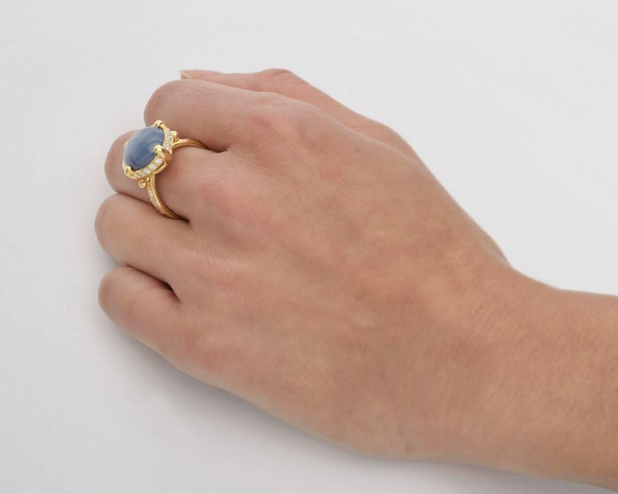 Cocktail ring, showcasing a bezel-set oval light blue star sapphire with good asterism, surrounded by round brilliant-cut diamonds and with partway round brilliant-cut diamond-set shoulders, in 18k yellow gold, signed Temple St. Clair. Star sapphire