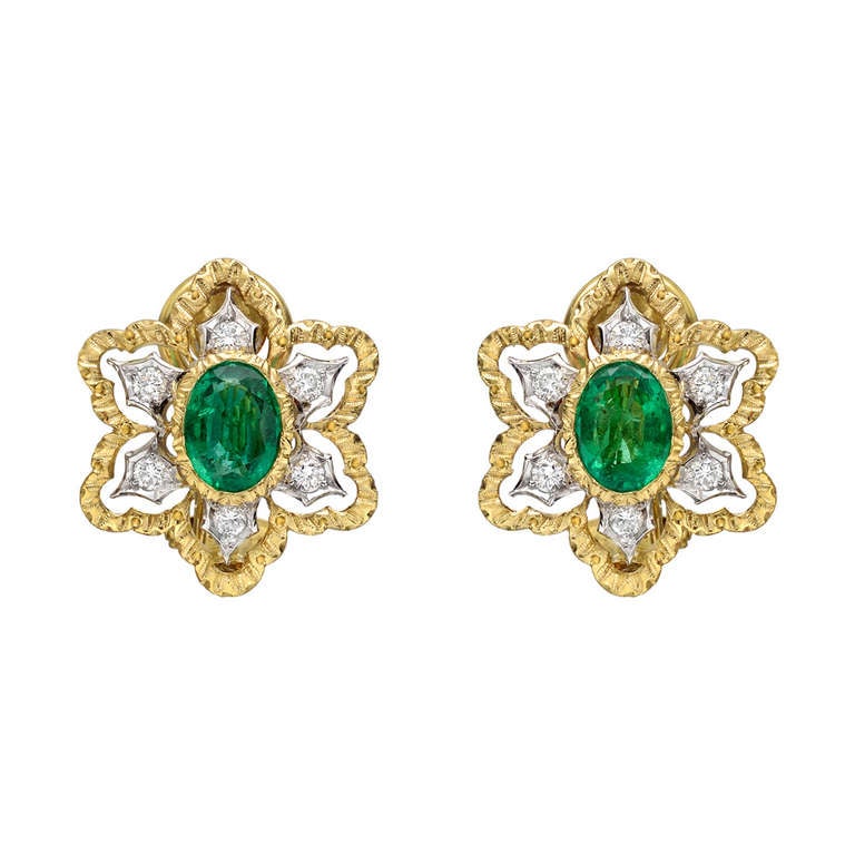 Emerald and diamond open foliate design earclips, centering on an oval-shaped emerald set in 18k yellow gold, with a circular-cut diamond surround set in pierced 18k white gold to an 18k yellow gold fringe, with clip backs, originally retailed by