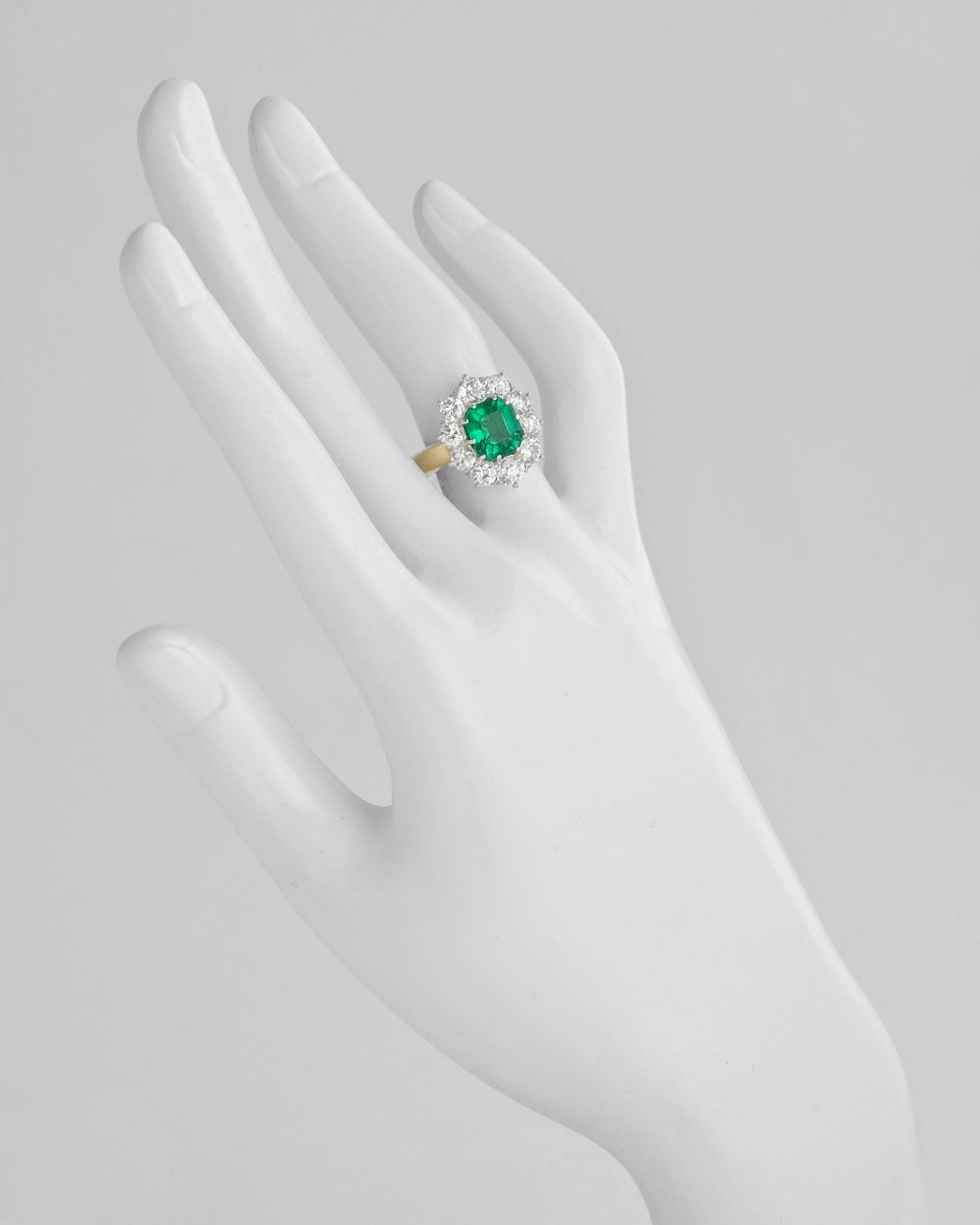 Emerald and diamond cluster ring, centering on an octagonal step-cut emerald weighing 2.86 carats, within a circular-cut diamond surround, the diamonds weighing approximately 1.80 total carats, mounted in 18k yellow gold and platinum. Accompanied by