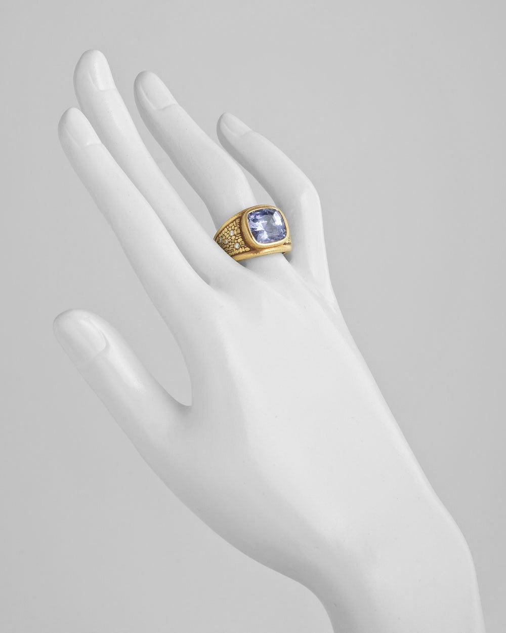 Cocktail ring, centering on a cushion-cut natural purple sapphire weighing approximately 7.12 carats, in a wide hand-engraved 18k yellow gold mounting with small round diamond accents at shoulders, originally retailed as new by Betteridge in 1995,