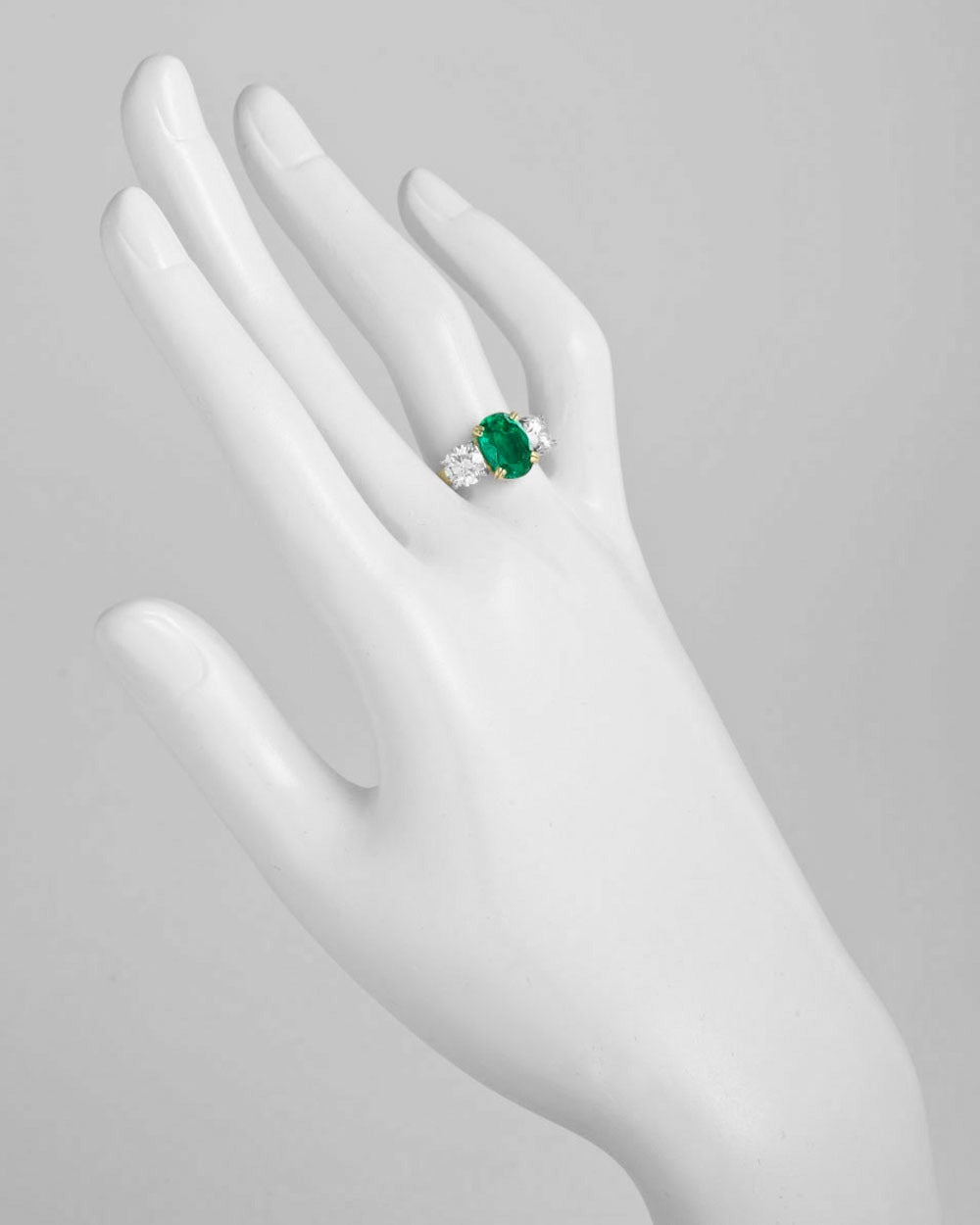 Colombian emerald and diamond three-stone ring, centering on an oval brilliant-cut emerald weighing 2.07 carats, flanked by two round brilliant cut diamond shoulders weighing 1.59 total carats (both G-color/SI2 clarity), mounted in 18k yellow gold