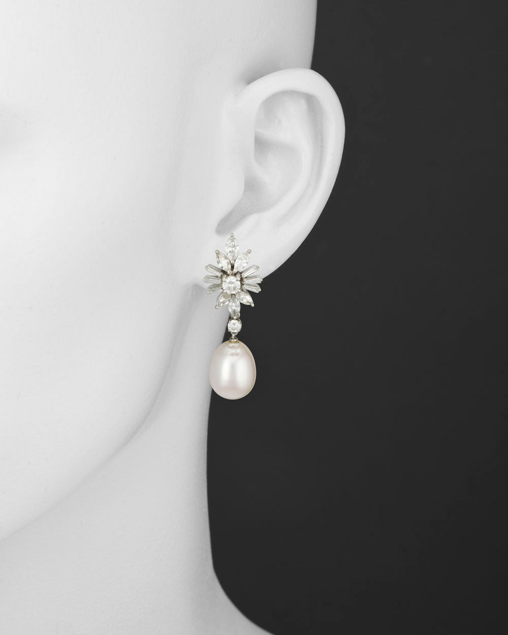 Pearl and diamond cluster pendant earrings, composed of a cultured pearl drop suspended from a marquise-shaped, baguette-cut and circular-cut diamond cluster surmount, mounted in platinum, with clip and post backs. 1.65