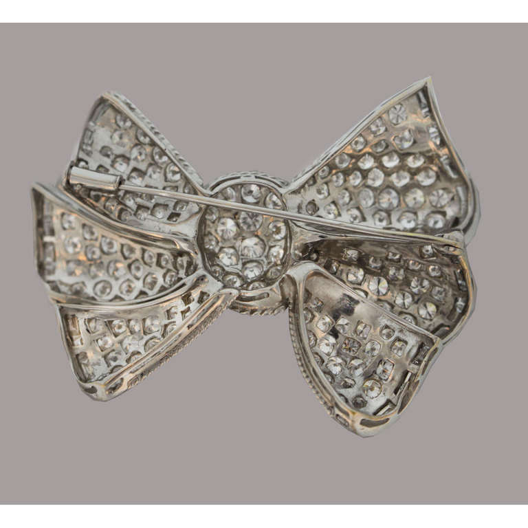 Retro bow-shaped pin, set with sparkling circular-cut diamonds, with a baguette-cut diamond border that adds graceful movement to the piece, the diamonds weighing approximately 16.00 total carats, circa 1950's, mounted in platinum. 2.25