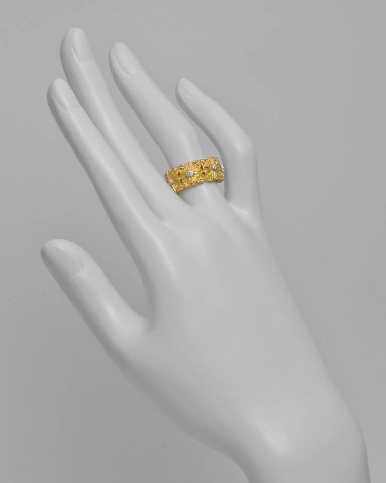 Cassetoni foliate-patterned band ring, designed with a sequence of seven engraved gold flower motifs forming the band, each flower accented by a single round-cut diamond at center in a white gold setting, the diamonds weighing approximately 0.14