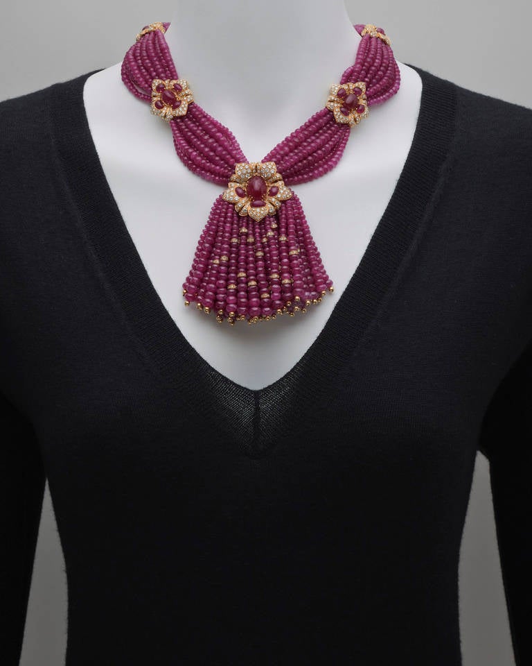 9-row ruby bead necklace, the beads gathered together by five cabochon-cut ruby and circular-cut diamond floret stations in 18k yellow gold, to the central graduated ruby bead and diamond-set 18k yellow gold rondelle multi-strand tassel pendant, the