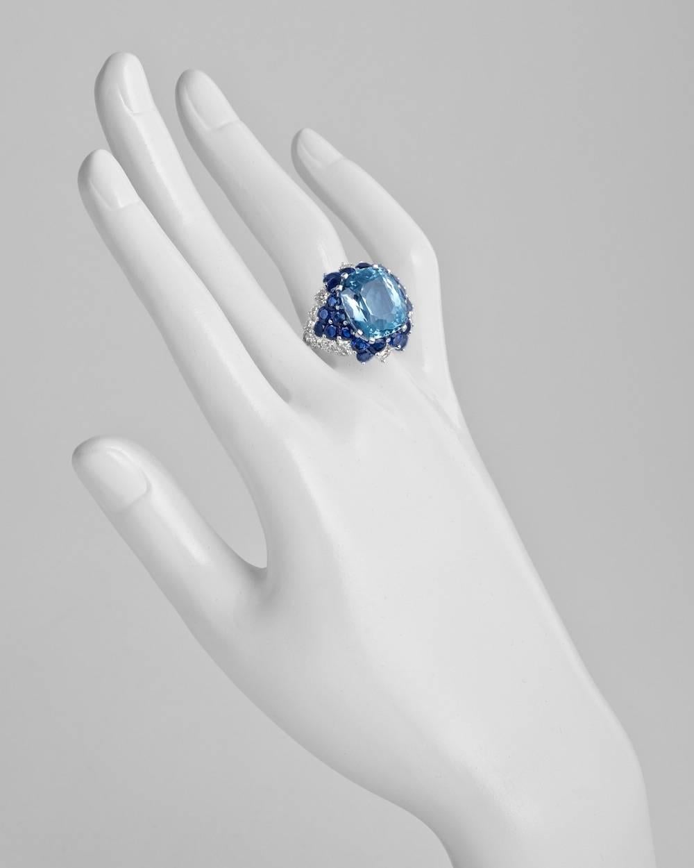 Gem-set cocktail ring, centering a cushion-cut aquamarine weighing approximately 9.74 carats, accented by a circular-cut sapphire and diamond surround of a flower petal motif, mounted in platinum. Sapphires weighing approximately 4.09 total carats