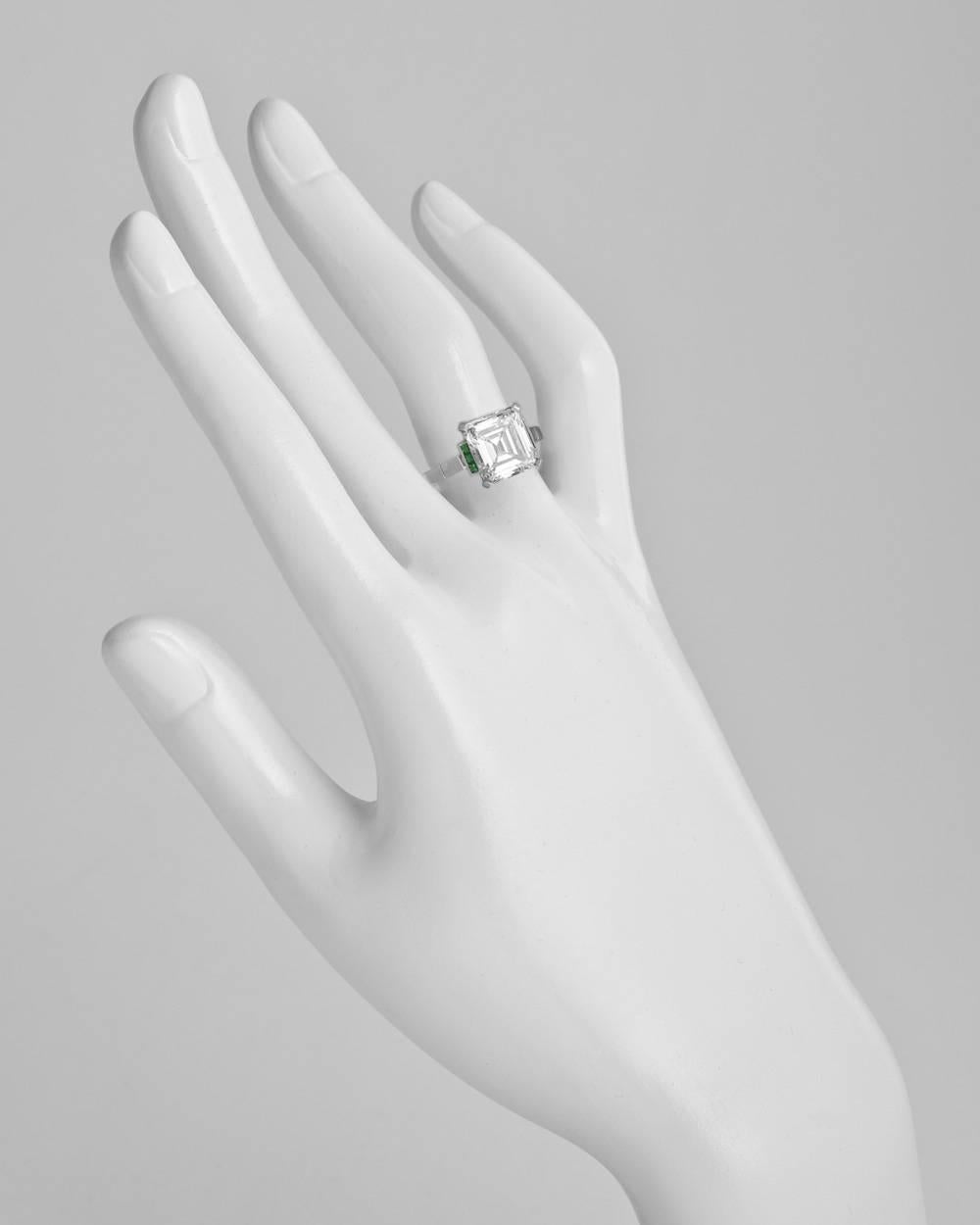 Diamond engagement ring, showcasing a colorless emerald-cut diamond weighing 3.43 carats (F-color/SI1-clarity), flanked by three step-cut emerald accents at the top of either shoulder, mounted in platinum. Six emeralds weighing 0.08 total carats.