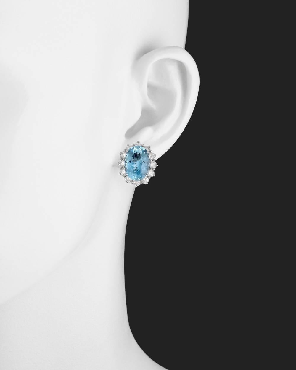 Cluster earrings, showcasing a larger oval-shaped aquamarine surrounded by round brilliant-cut diamonds, mounted in platinum.  Two aquamarines weighing 10.76 total carats and twenty-four diamonds weighing 2.84 total carats. Omega-style clip backs