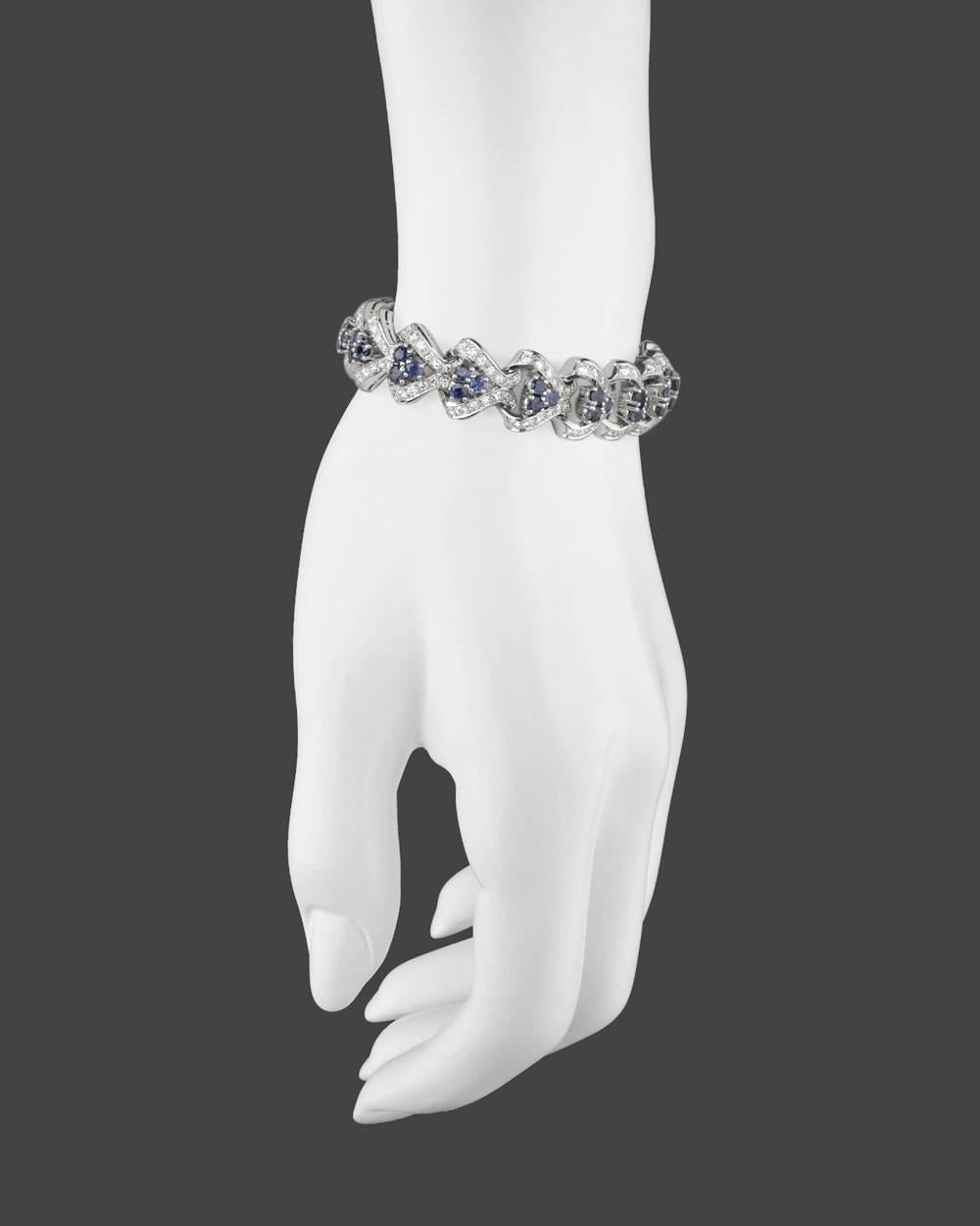 Sapphire and diamond scroll bracelet, each arrow-shaped link set with a trefoil cluster of round sapphires flanked by a row of round diamonds on either side, in 18k white gold. 51 sapphires weighing approximately 6.12 total carats and 170 diamonds