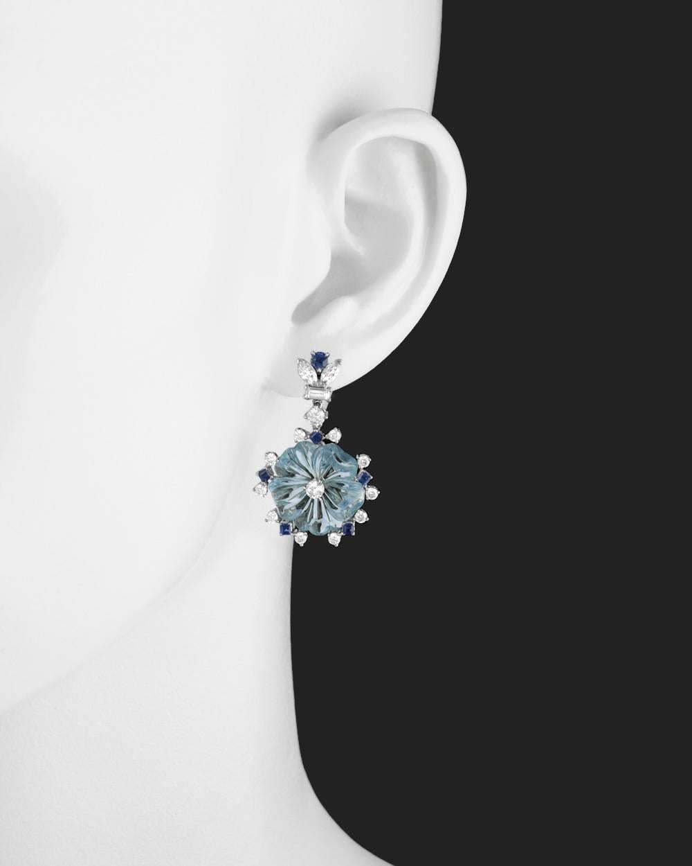Pendant earrings, showcasing a larger aquamarine carved in the shape of a five-petaled flower centering a round brilliant-cut diamond, the flower motif surrounded by a round diamond and sapphire border, with an elegant round, marquise and