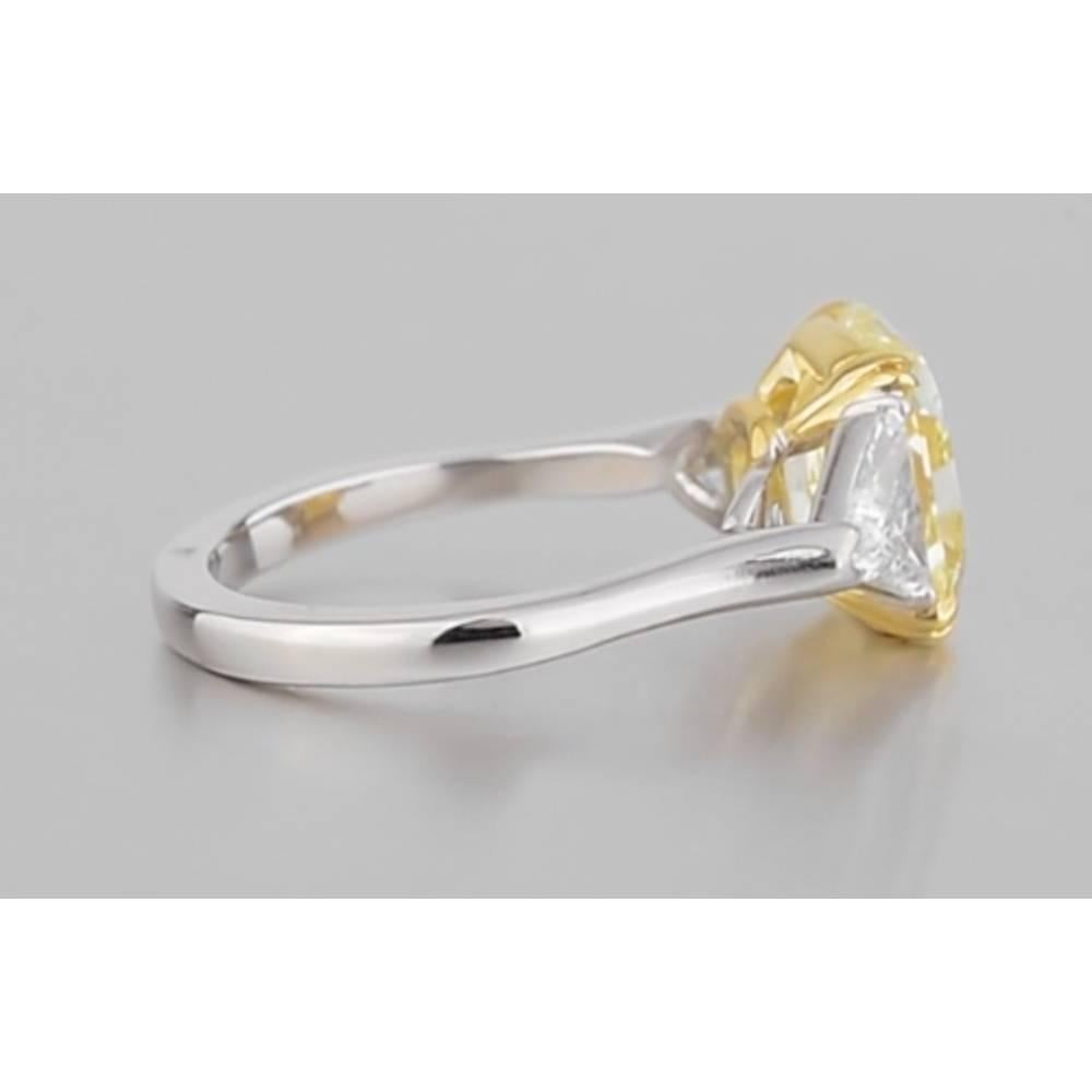 Yellow diamond engagement ring, centering a radiant-cut fancy yellow diamond weighing 4.20 carats, flanked by trillion-cut white diamond shoulders weighing approximately 1.20 total carats, mounted in platinum with an 18k yellow gold central basket.