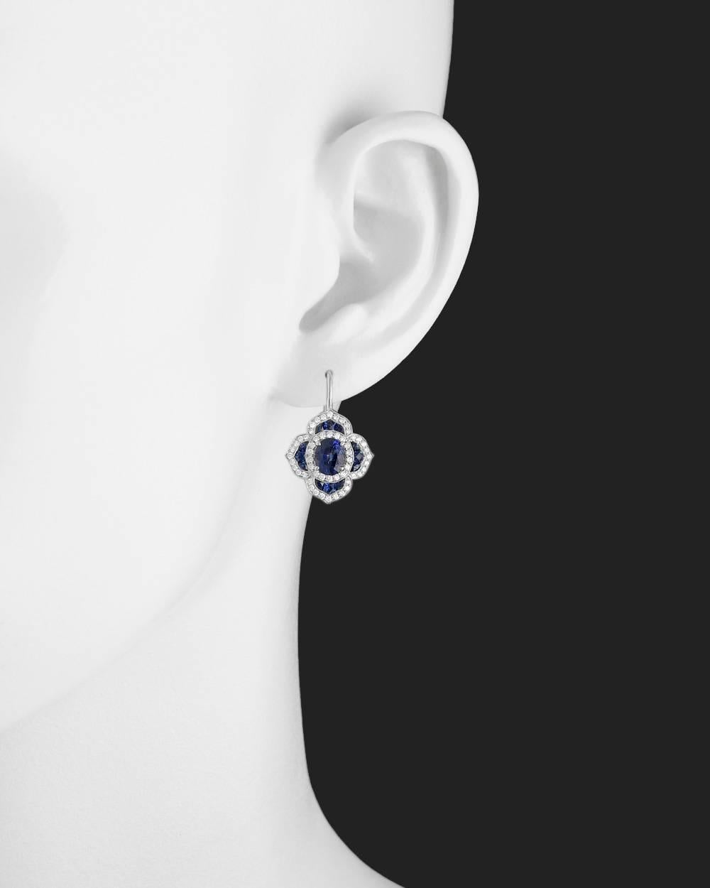 Sapphire and diamond foliate cluster drop earrings, centering a larger oval-shaped sapphire surrounded by round-cut diamonds to the calibre-cut sapphire and round-cut diamond scalloped border, mounted in platinum. Two oval-shaped sapphires weighing