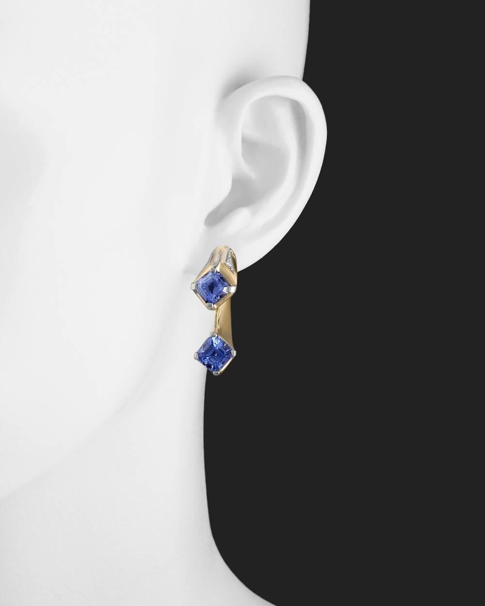 Retro earclips, showcasing a double trumpet motif with light blue emerald-cut sapphire terminals and near-colorless round brilliant-cut diamond accents, in polished 18k yellow gold and platinum. Four sapphires weighing approximately 8.16 total