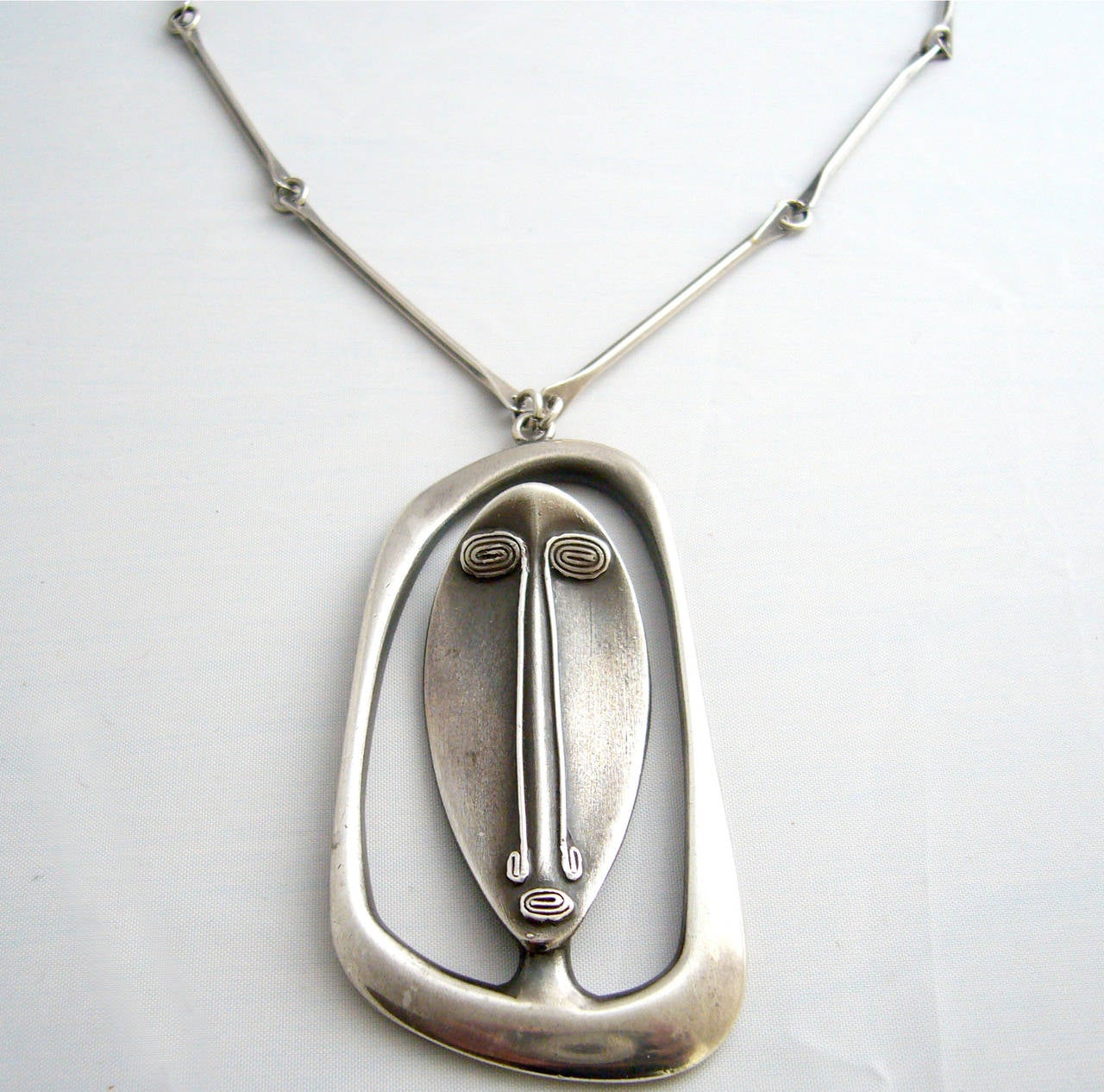 A 1950s sterling silver mask necklace created by Irvin and Bonnie Burkee of of Arizona. Necklace is comprised of a large modernist mask pendant measuring 3.25