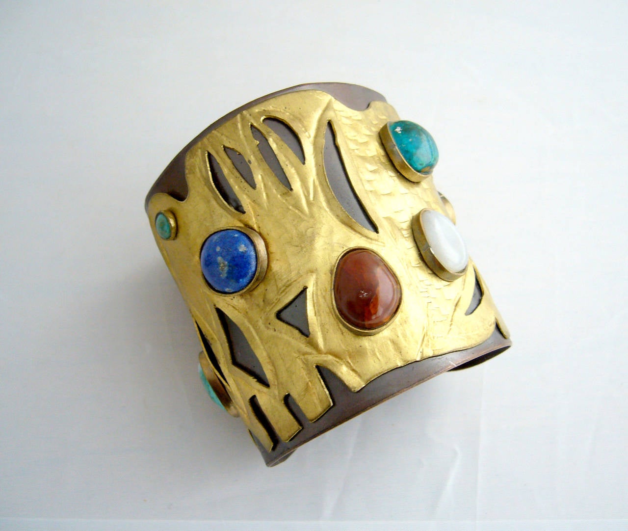 A handmade bracelet comprised of a uniquely hammered brass plate mounted on copper featuring nine semi-precious gemstones which include lapis, malachite and what appears to be agate and quartz by Juan Reyes of Chile. Cuff measures 3