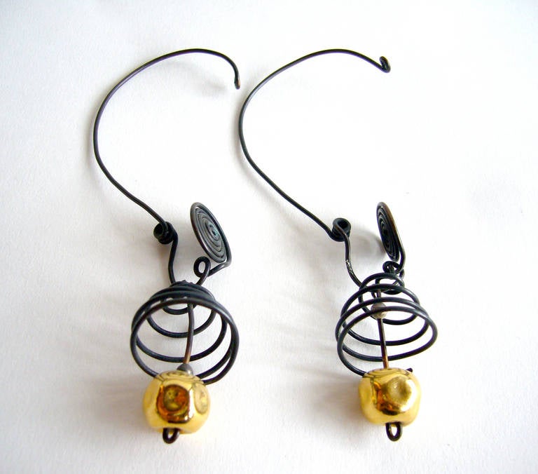 Hand made, one of a kind earrings designed and created by Margret Craver Withers of Kansas.  Earrings are comprised of blackened, spiraling wire that create a cage for a golden kinetic bead.  Earrings are quite clever in that they are designed for