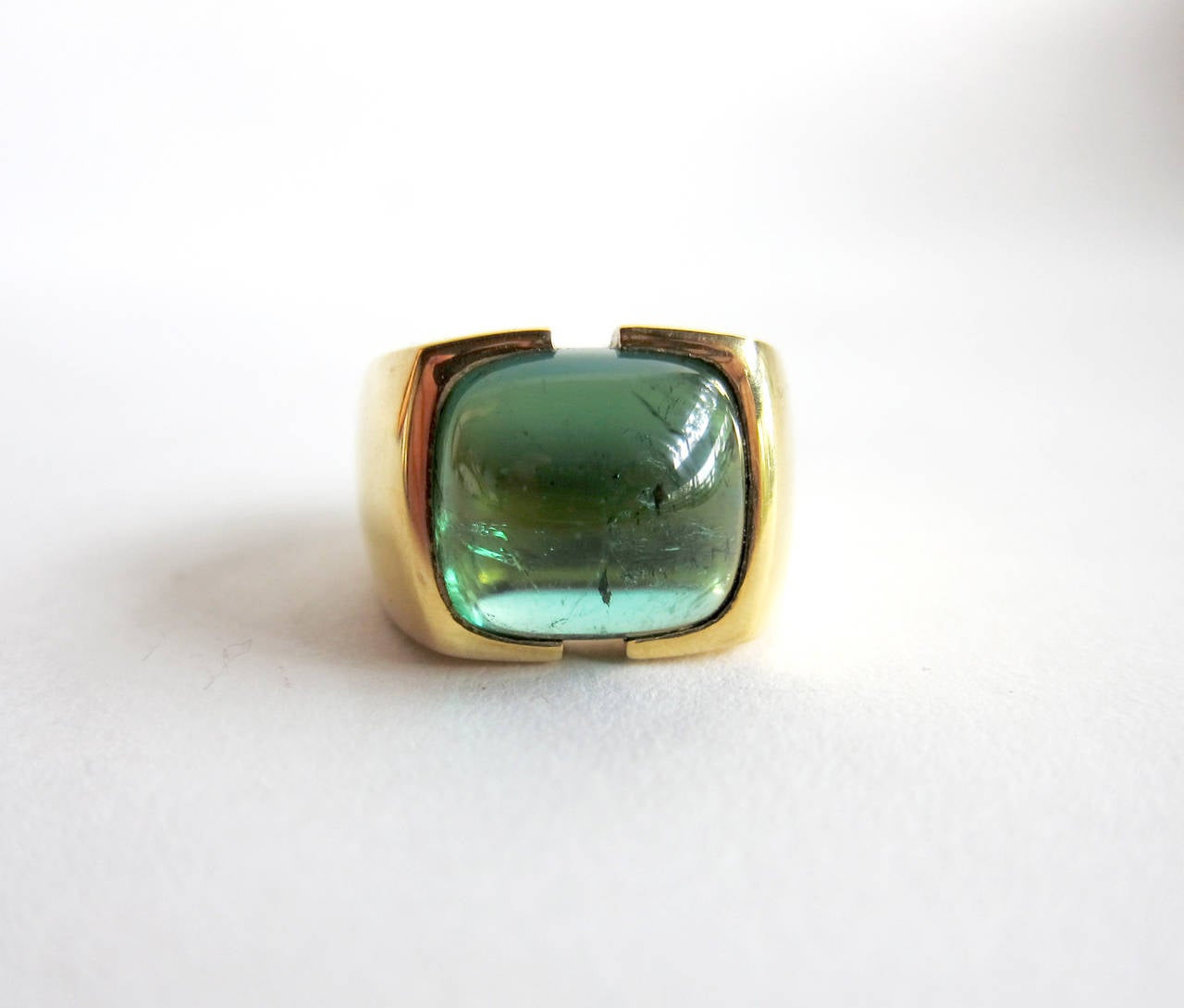 An 18K gold mounting centering a large cushion-shape green tourmaline cabochon ring, circa 1970s. Ring is signed 18k and is a size 9 3/4 and , suitable for a man or woman.  Weighs a hefty 34.3 grams.  Excellent condition with natural inclusions in