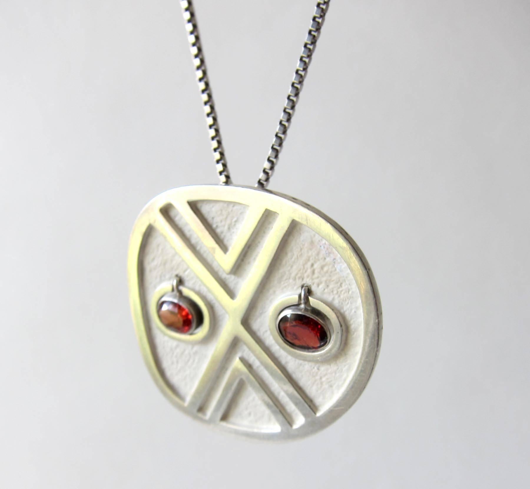 Silver pendant necklace with kinetic, hanging garnet eyes created by Oswaldo Guayasamin of Ecuador.  Pendant measures 1.5